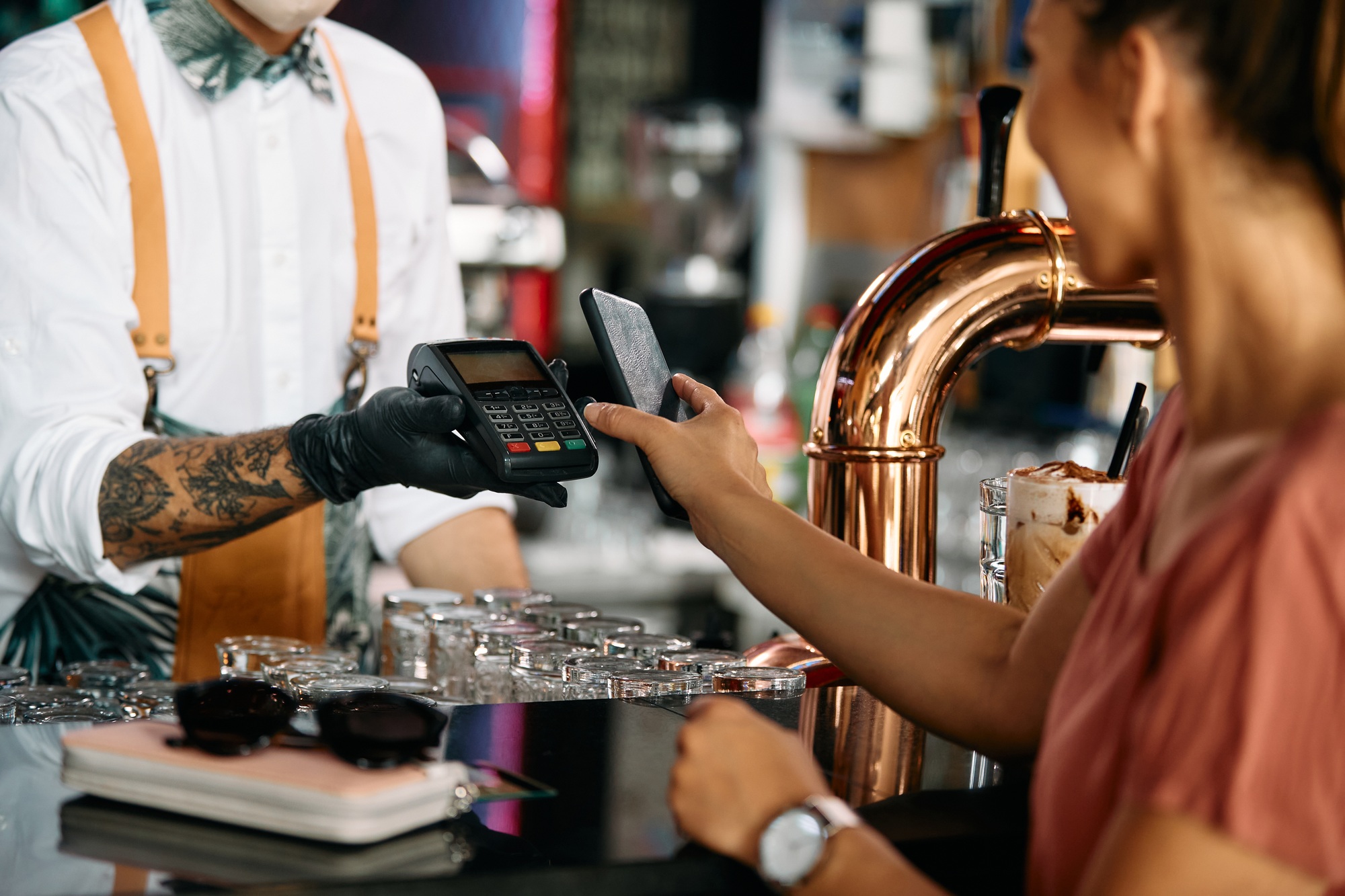 Close up of woman using mobile phone while paying at bar counter.