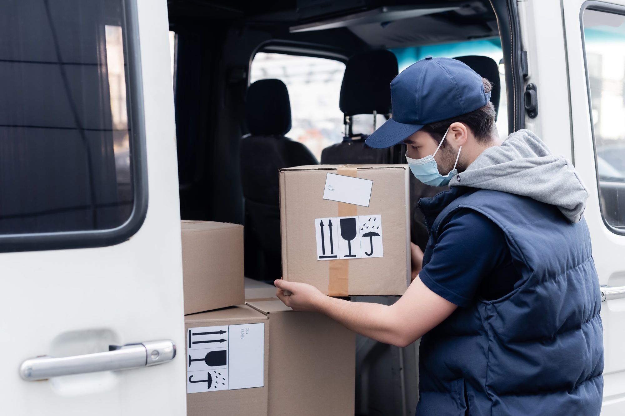 Courier in medical mask taking box from auto outdoors
