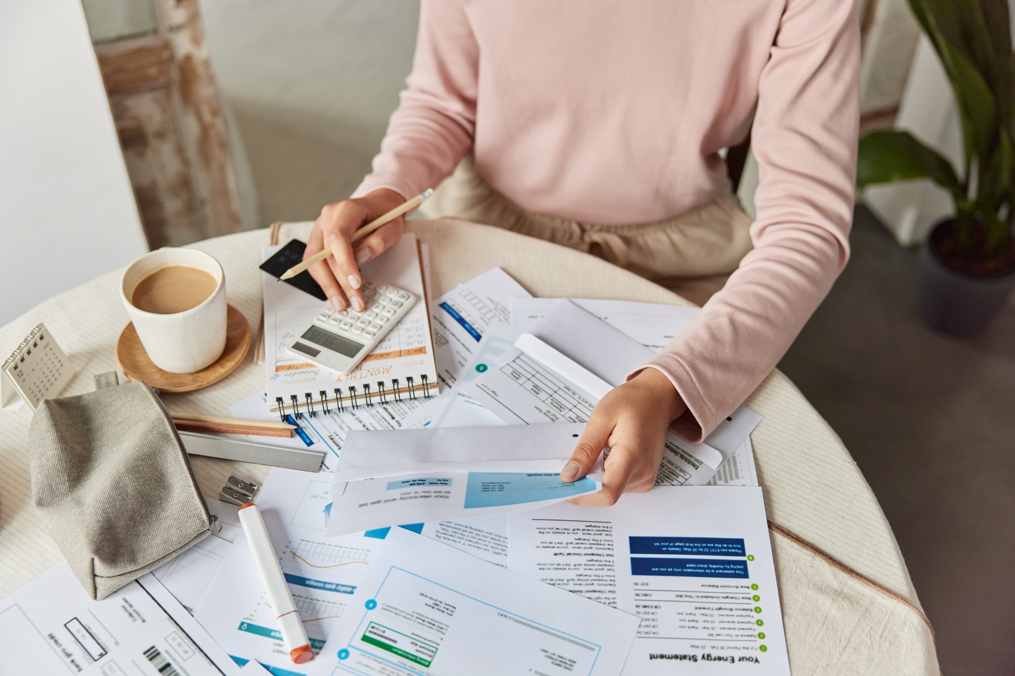 Cropped shot of unrecognizable woman calculates goods service price paying bills sits at round table