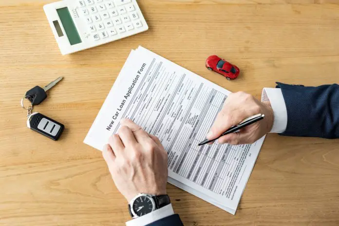 cropped view of car dealer holding pen near contract, calculator, toy car and car key