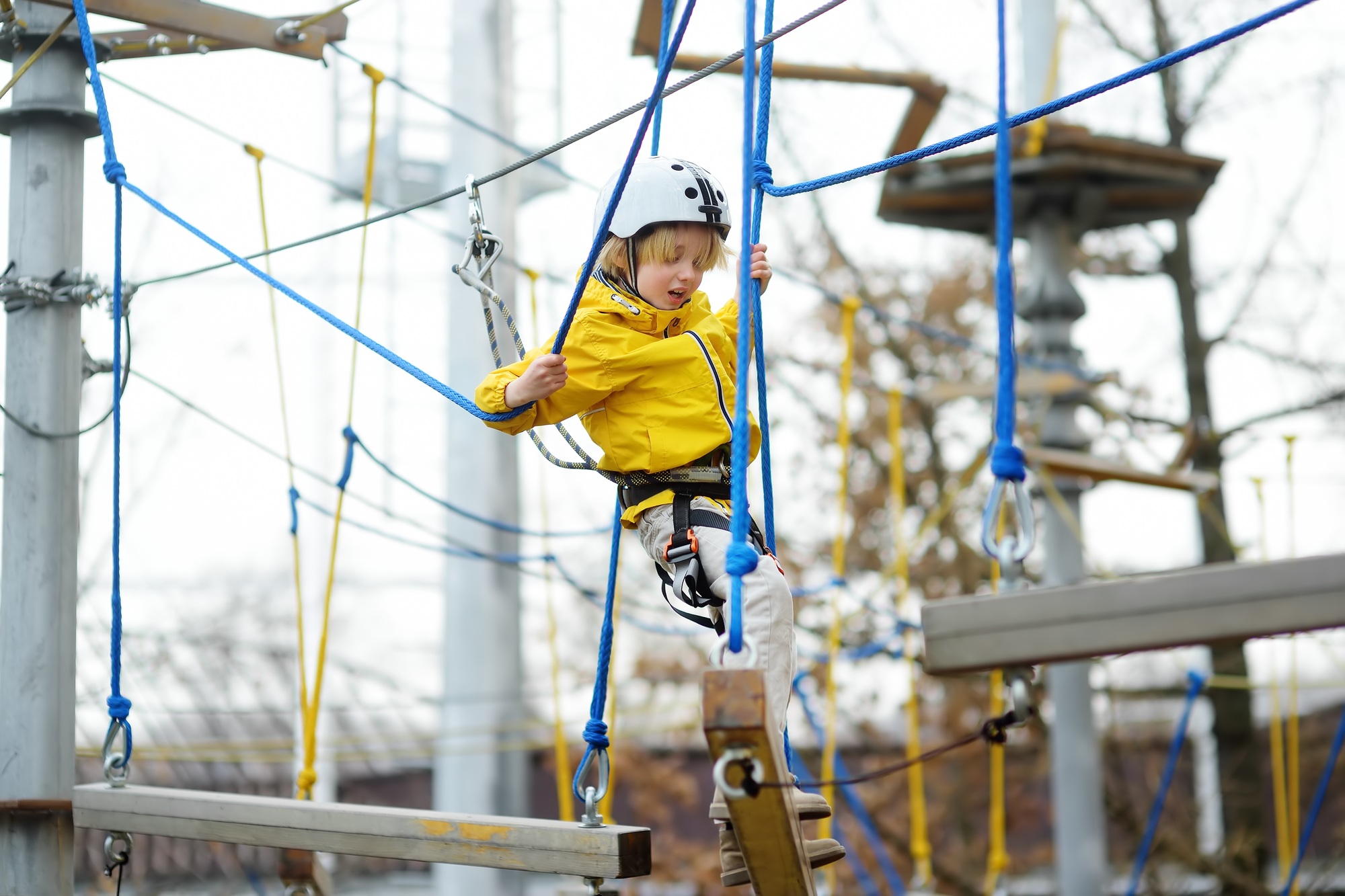 Cute boy having fun in Adventure Park for children amoung ropes, stairs, bridges. Frightened child