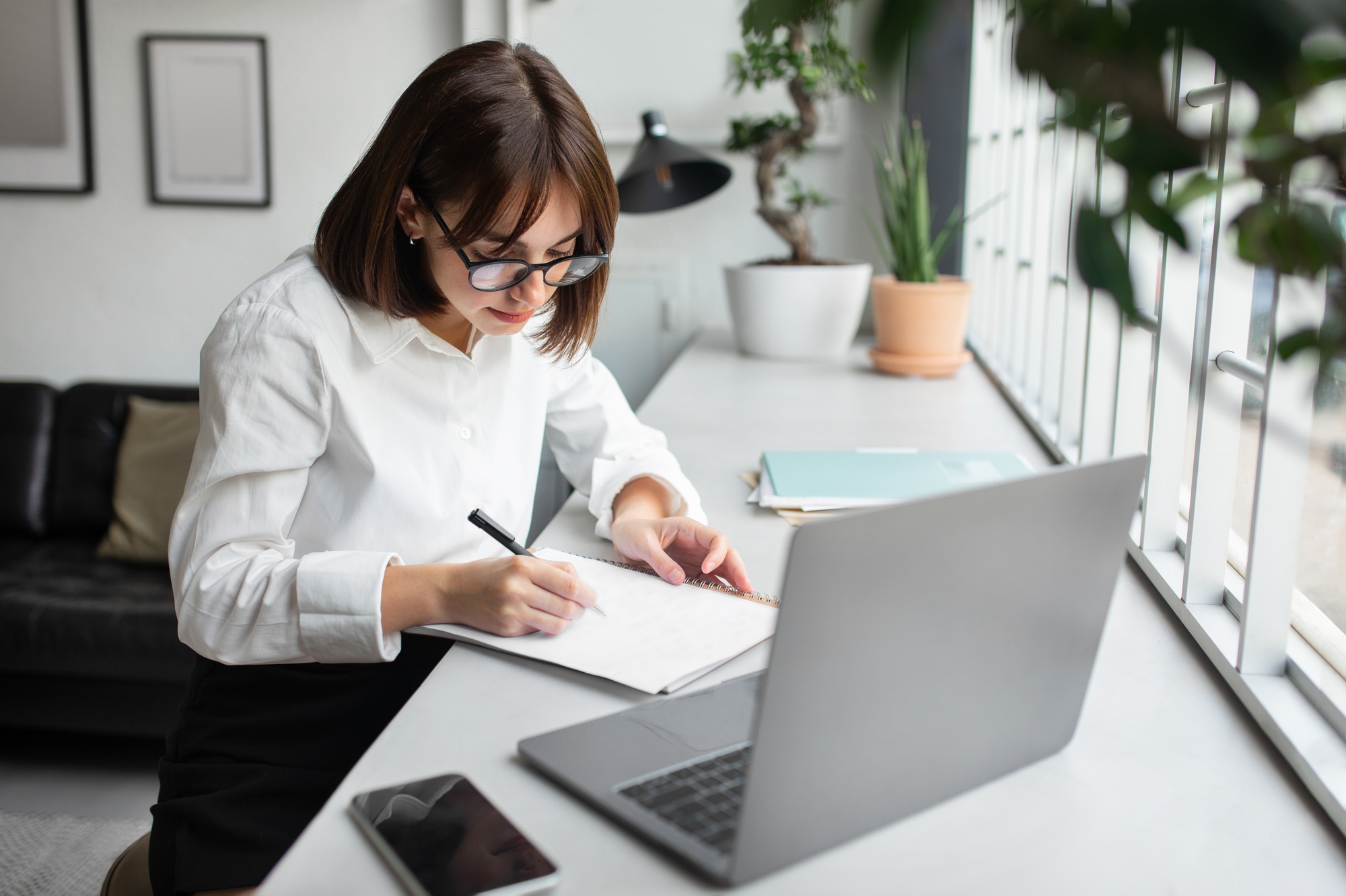 Entrepreneurship. Focused young businesswoman working using laptop and taking notes writing report