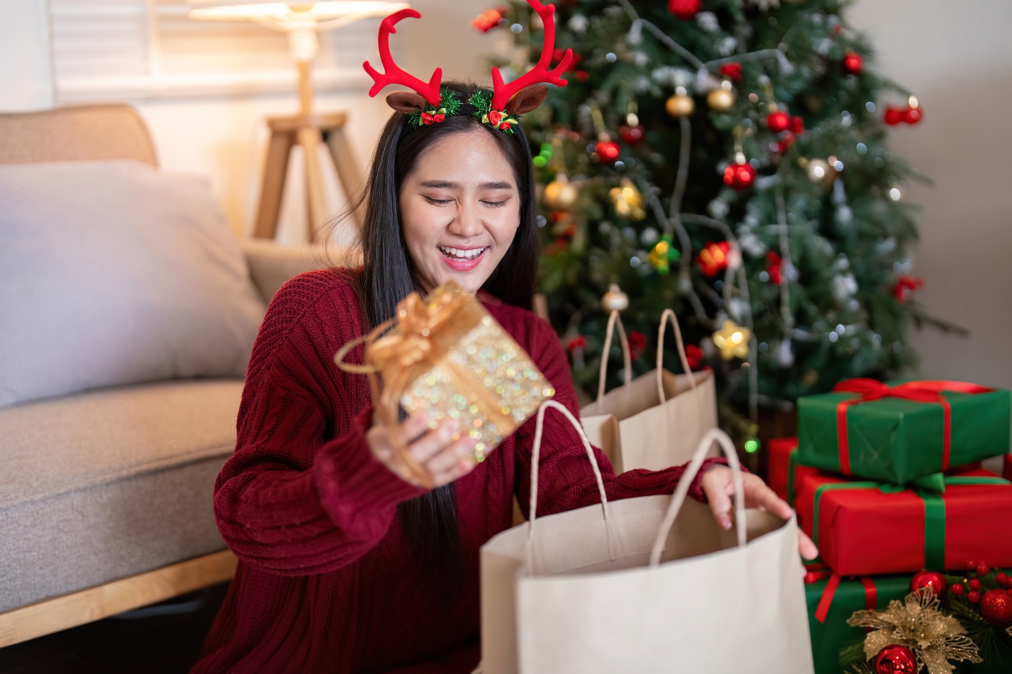 Excited Woman Discovering Surprises in Holiday Gift Box Near Festive Decor