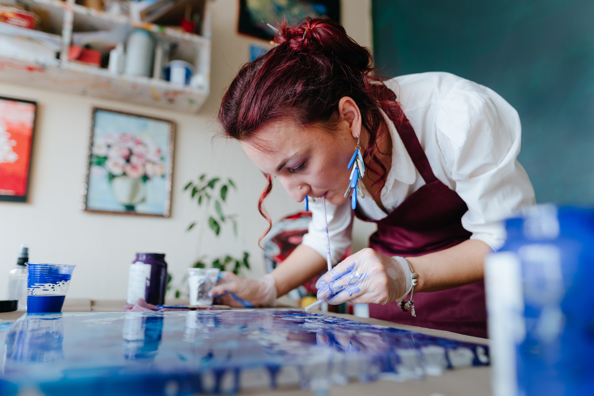Female artist mixing acryl paints on the picture using straw working in fluid art technique