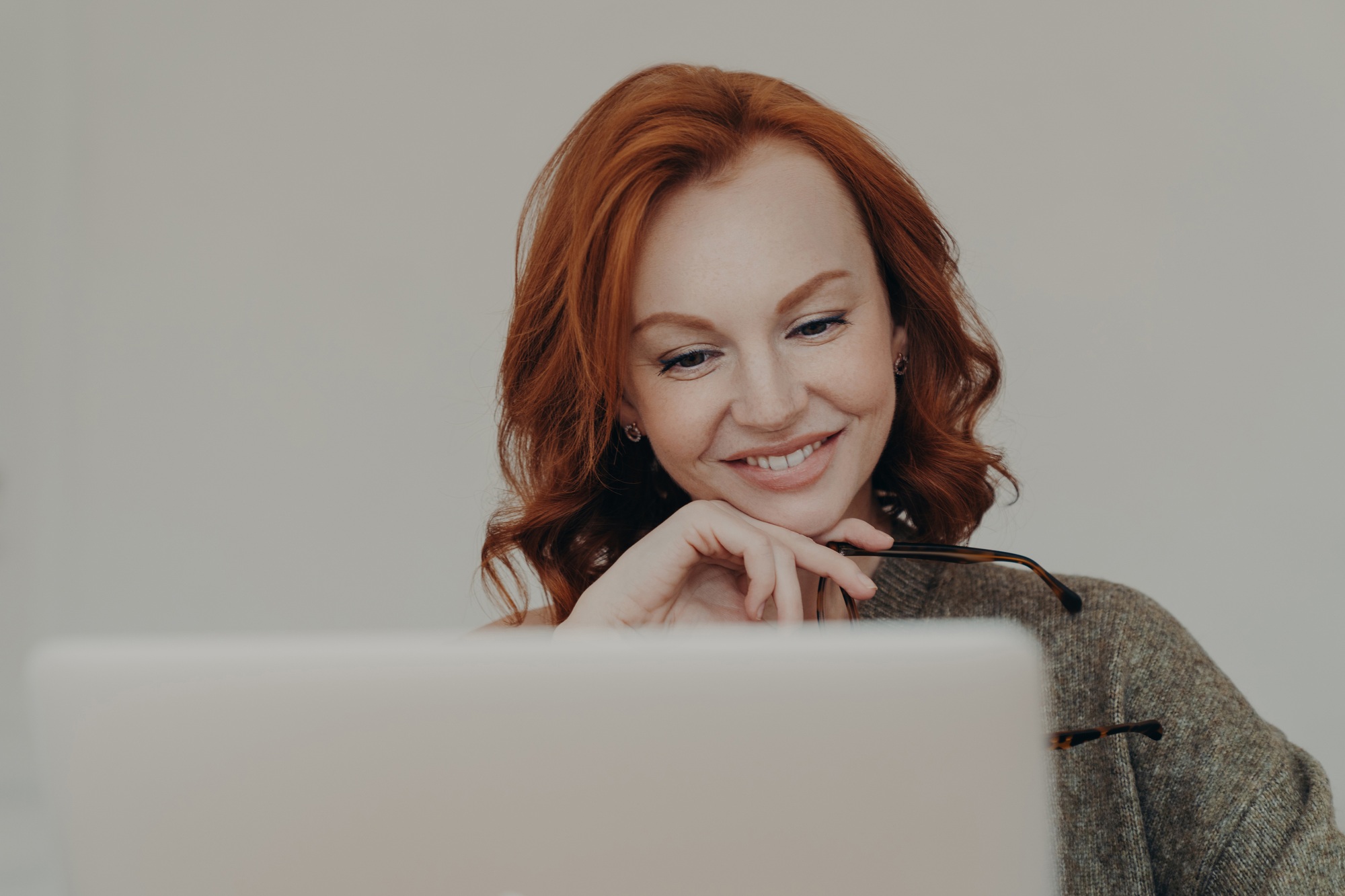 female student with ginger hair and pleasant smile watches interesting tutorial video or webinar