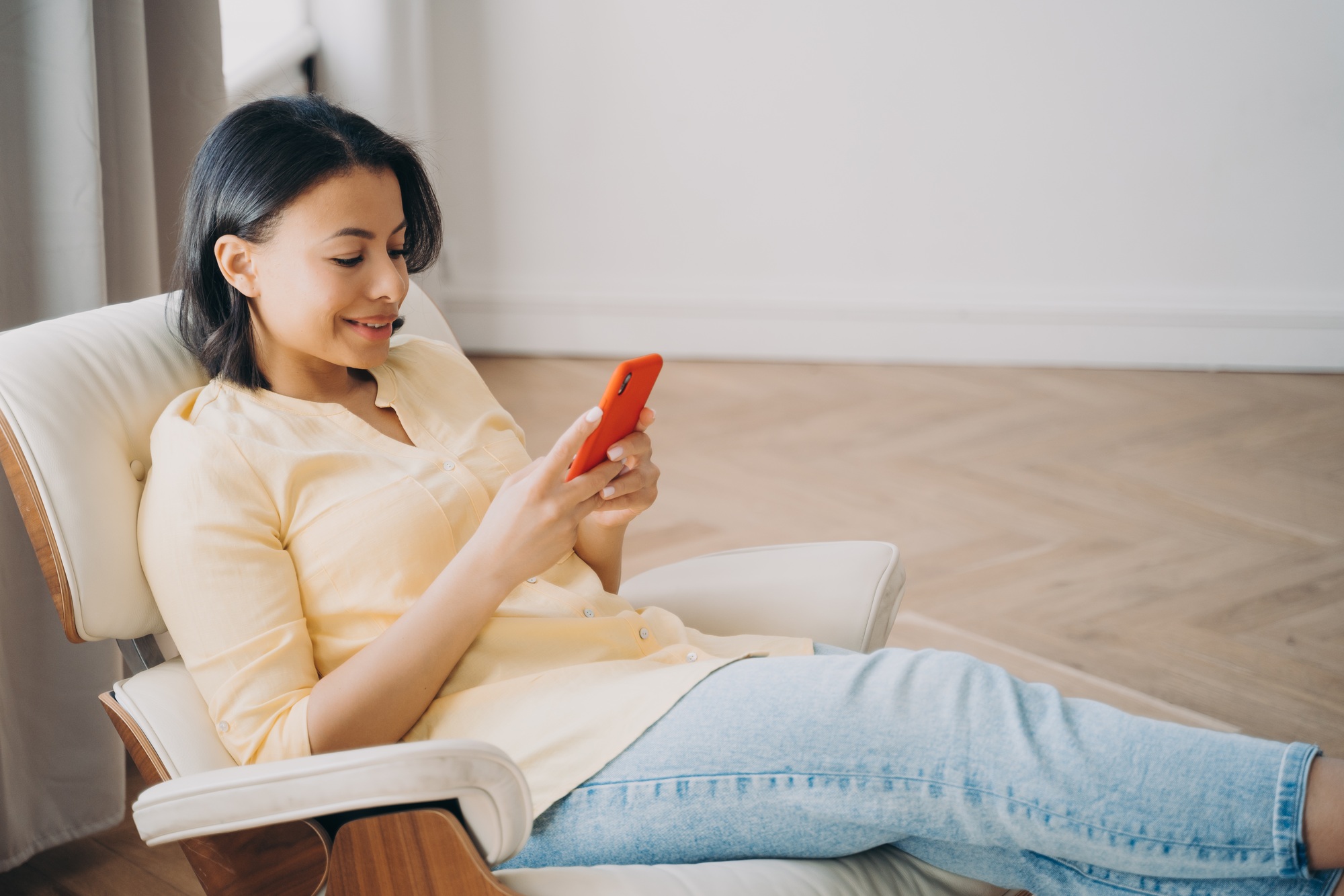Female using phone sitting in comfortable armchair at home, shopping online. Mobile apps advertising