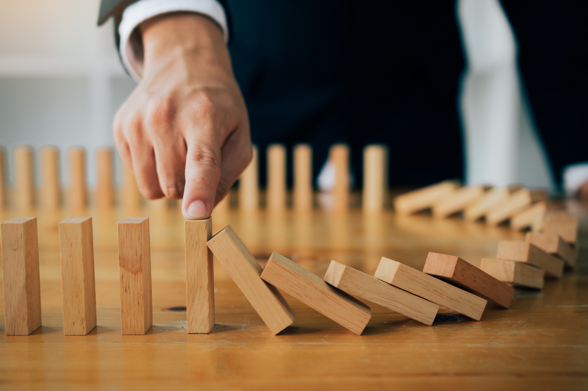 finger businessman stopping wooden block from falling in the line of domino