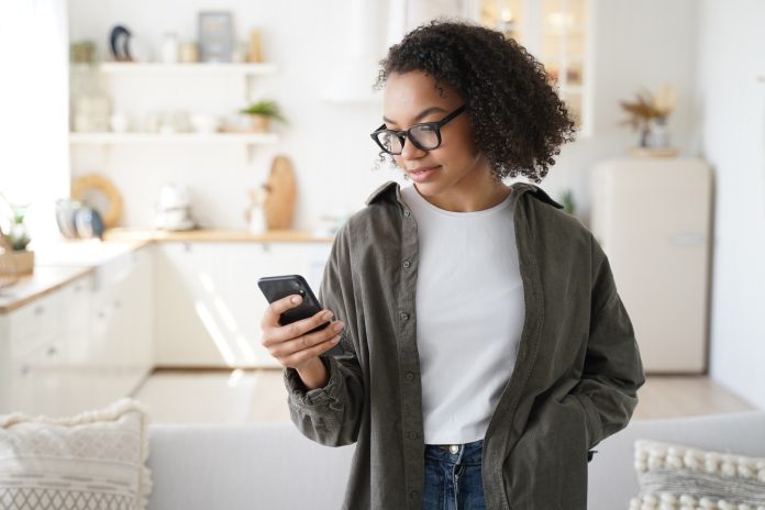 Focused young girl using smartphone at home, shopping groceries in online store with mobile apps