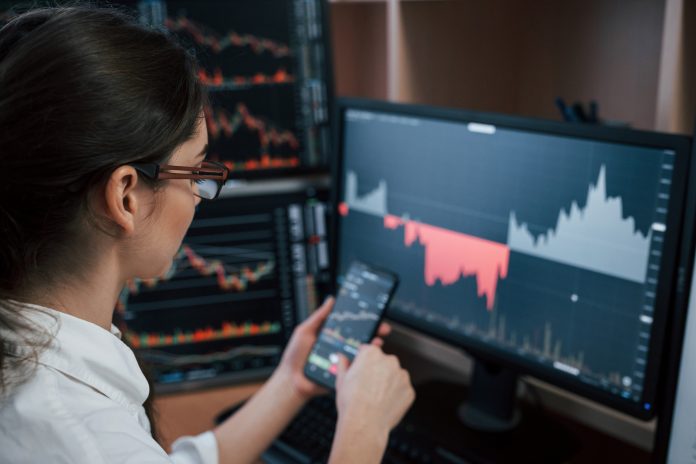 Full of job. Woman working online in the office with multiple computer screens in index charts