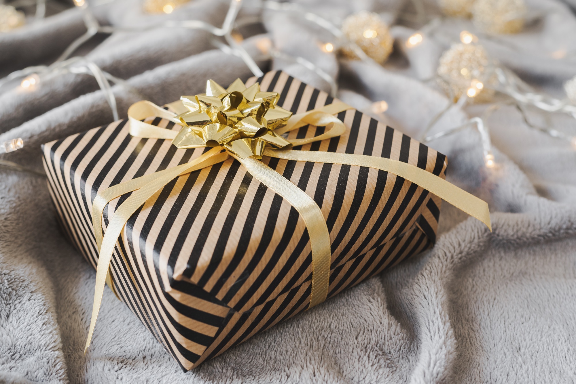 Gift box wrapped in craft paper with golden ribbon and bow. Christmas present wrapping idea