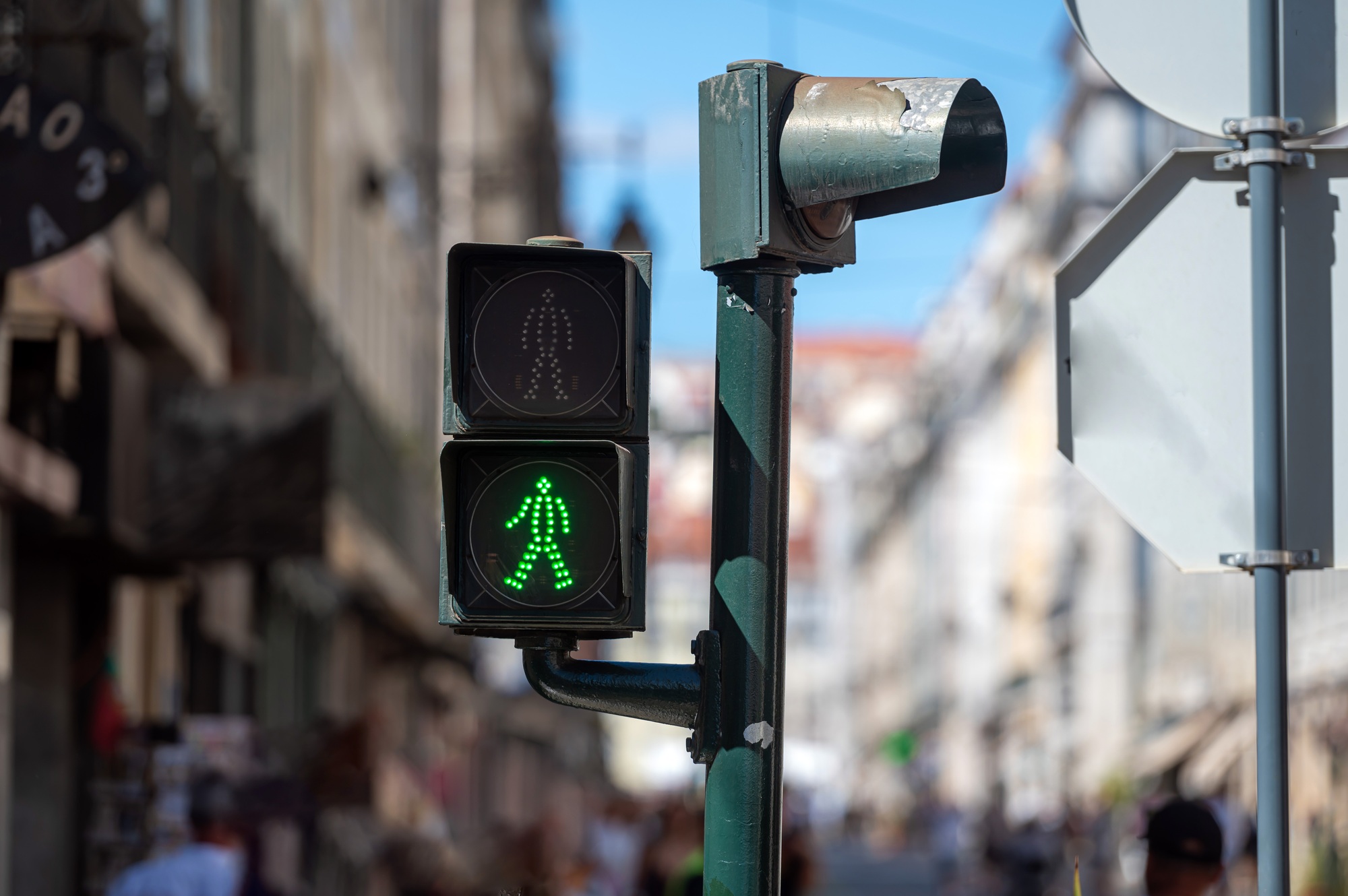 Green pedestrian signal guides foot traffic on a busy city street during daylight hours