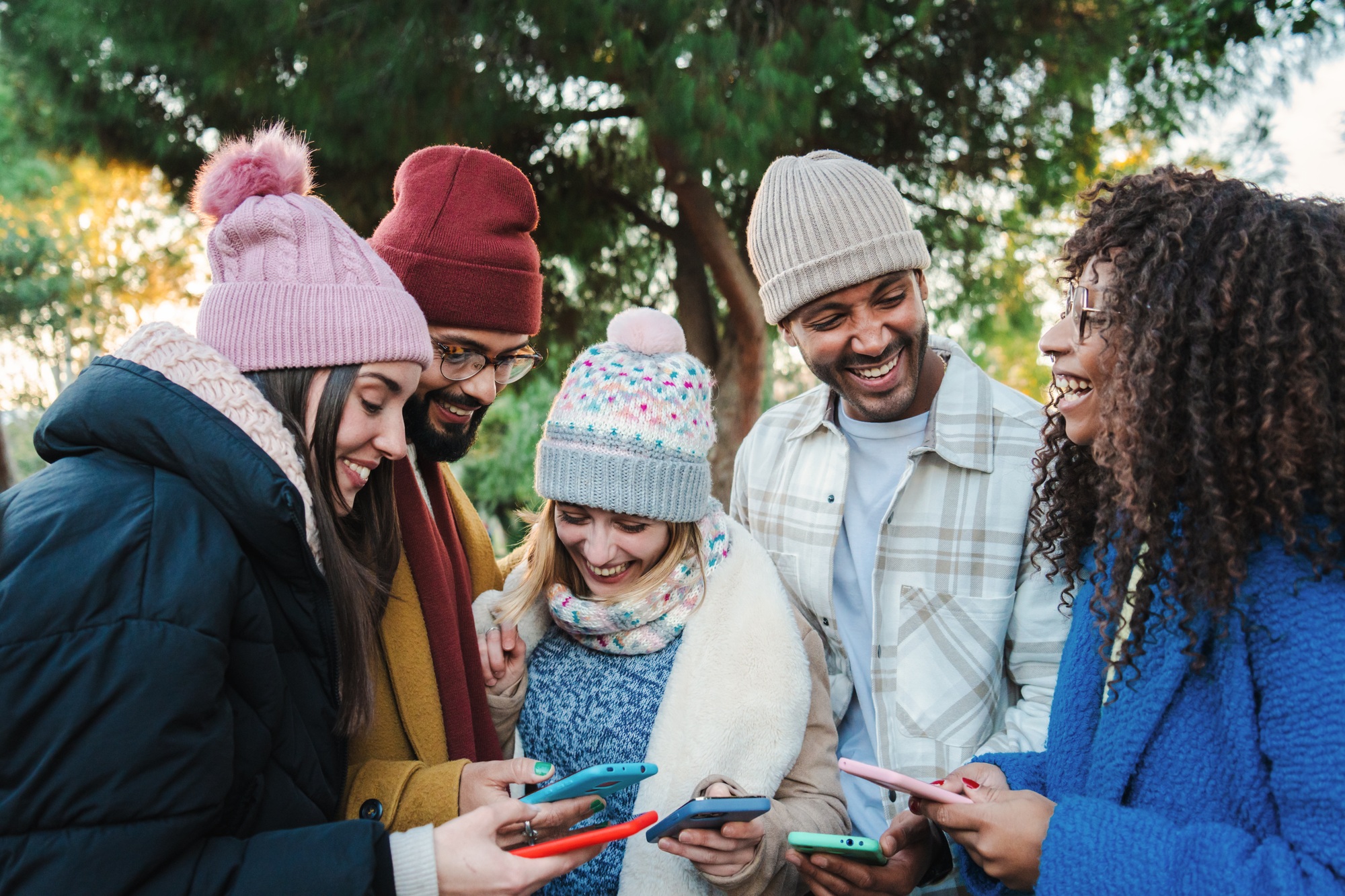 Group of multiracial young friends with coats and hats, smiling and watching the social media with a