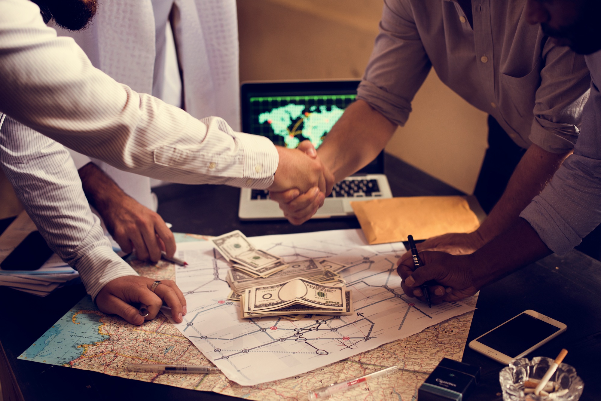 Group of people making agreement handshaking over map and money