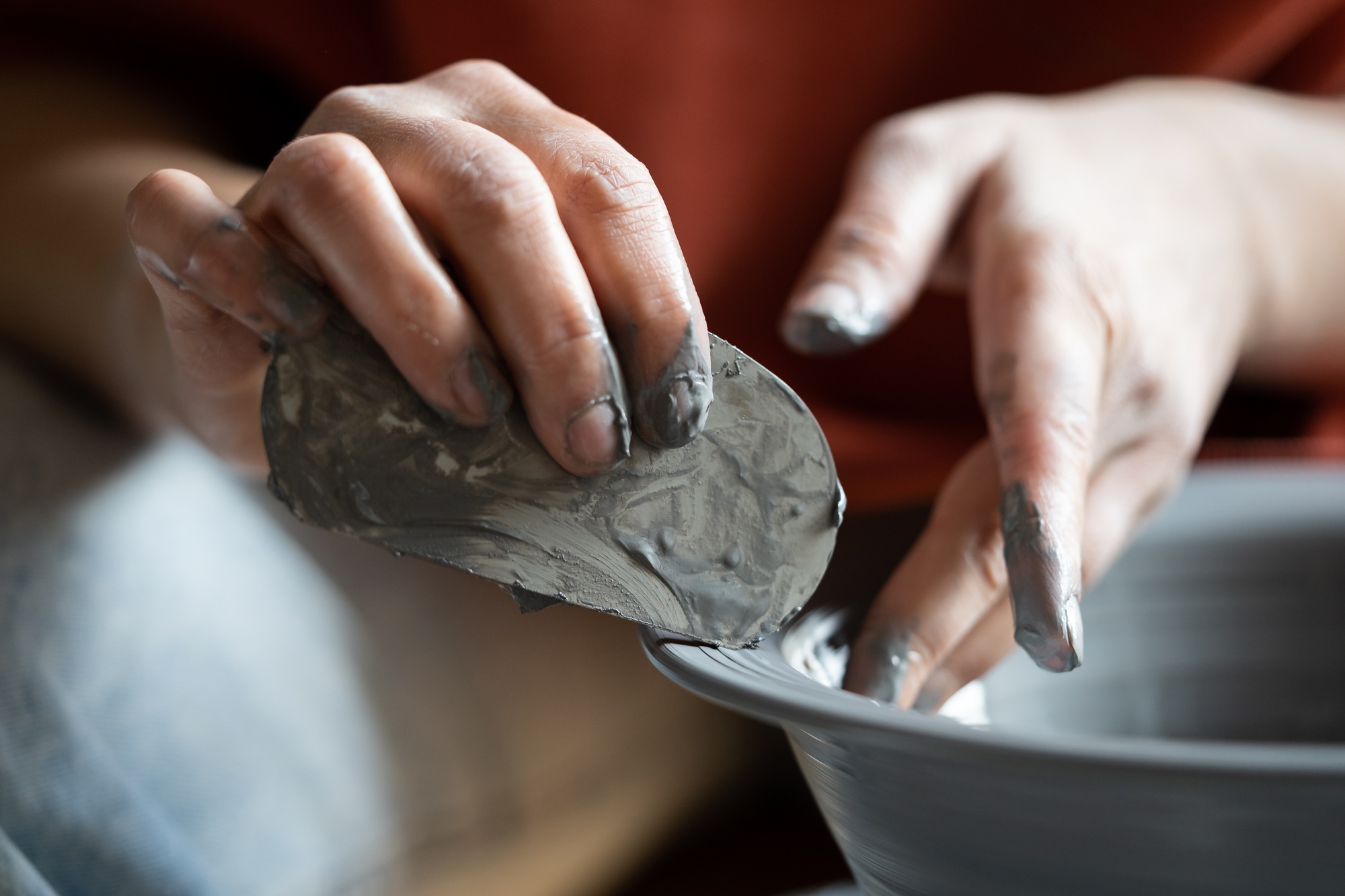 Hands of crafts woman shaping clay vessel with scraper during production of author dishes for sale