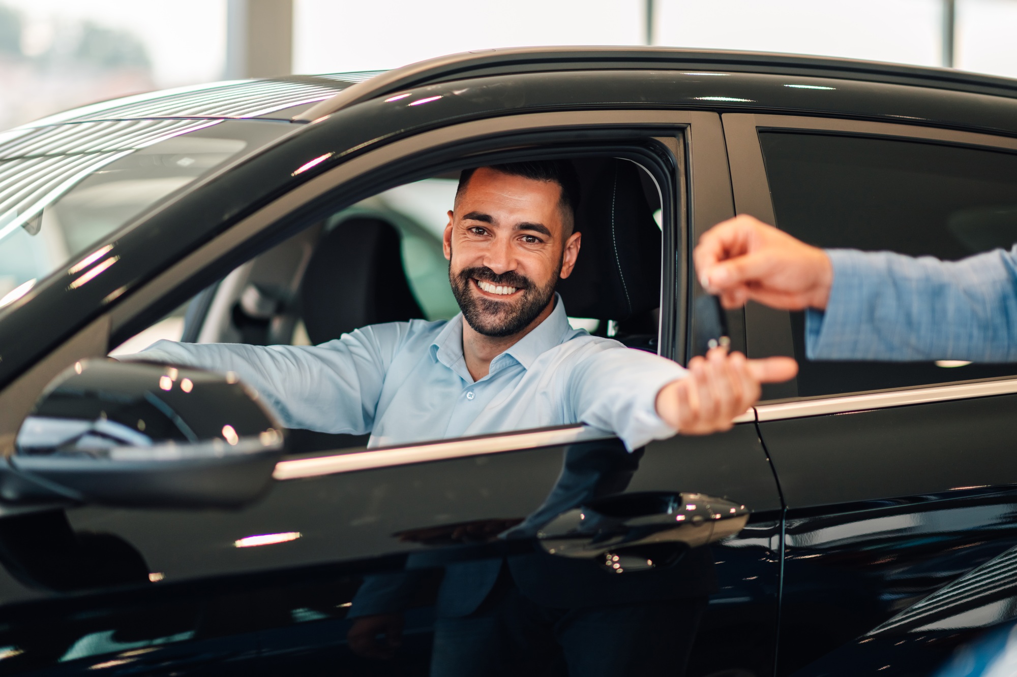 Happy man receiving car keys from another person in showroom.