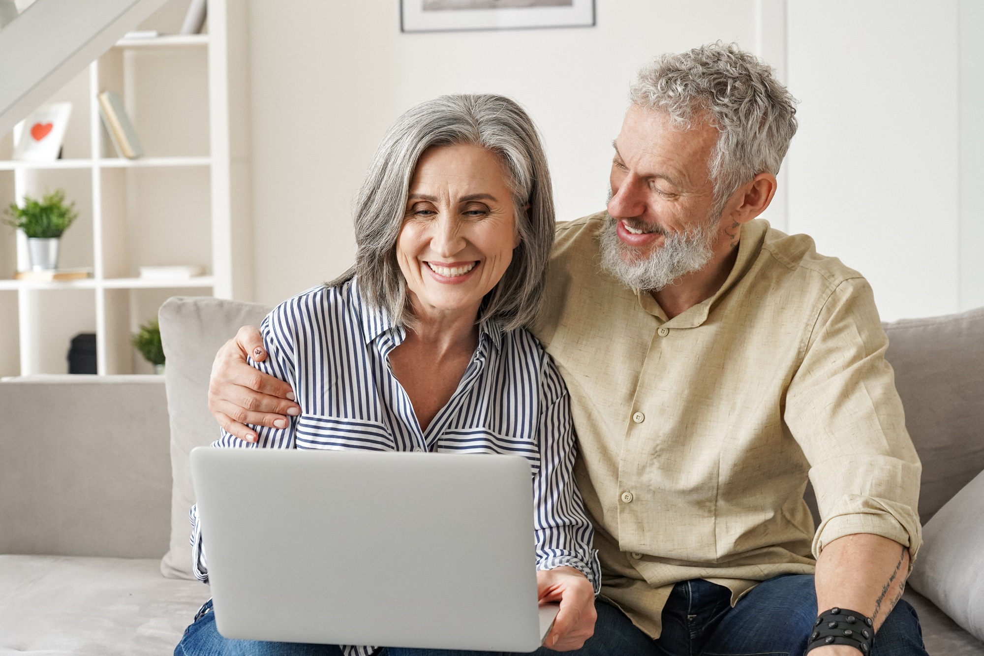 Happy mature mid age couple doing ecommerce shopping using laptop at home.