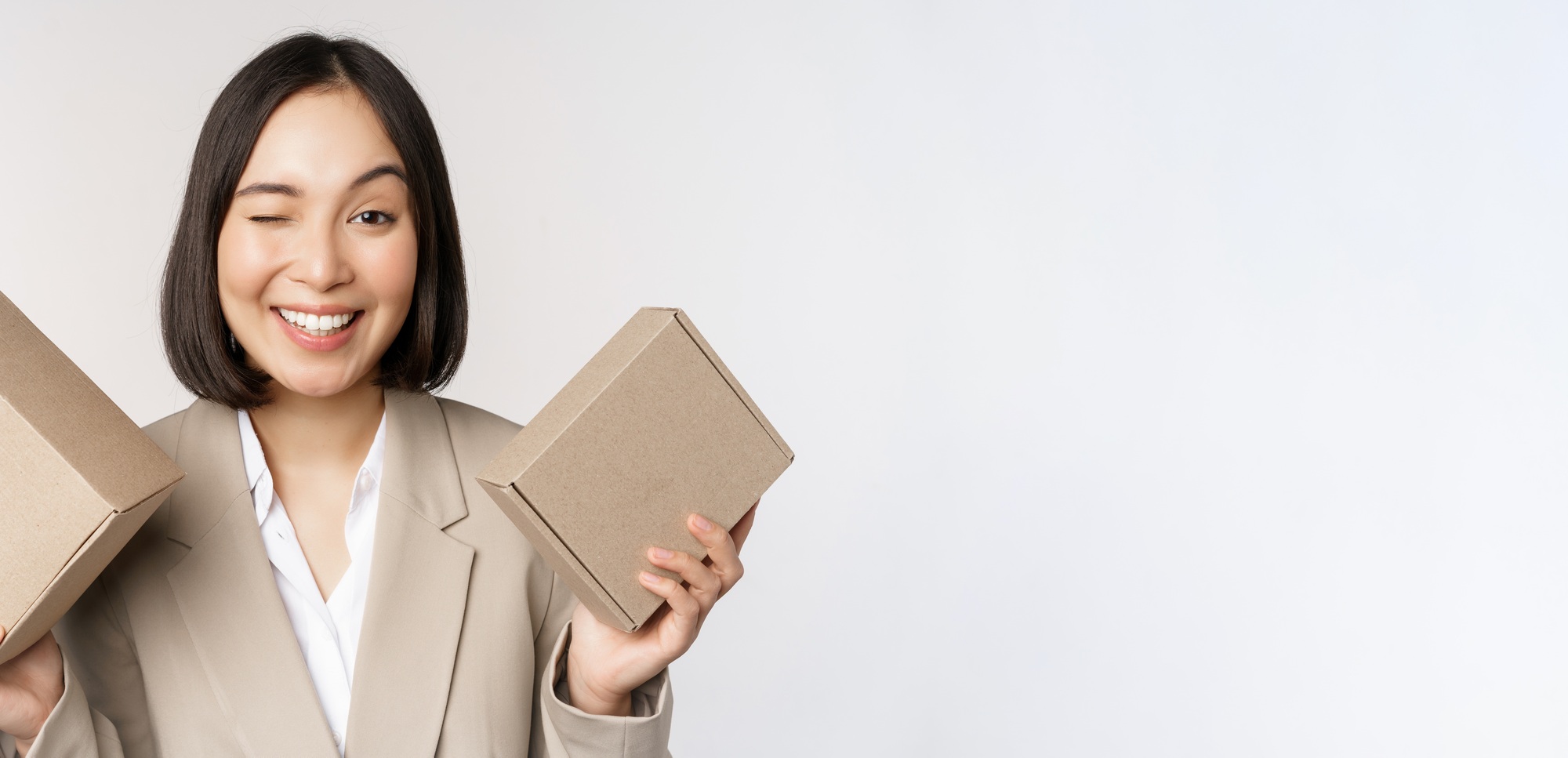 Image of saleswoman, asian businesswoman holding boxes with company brand product, smiling at