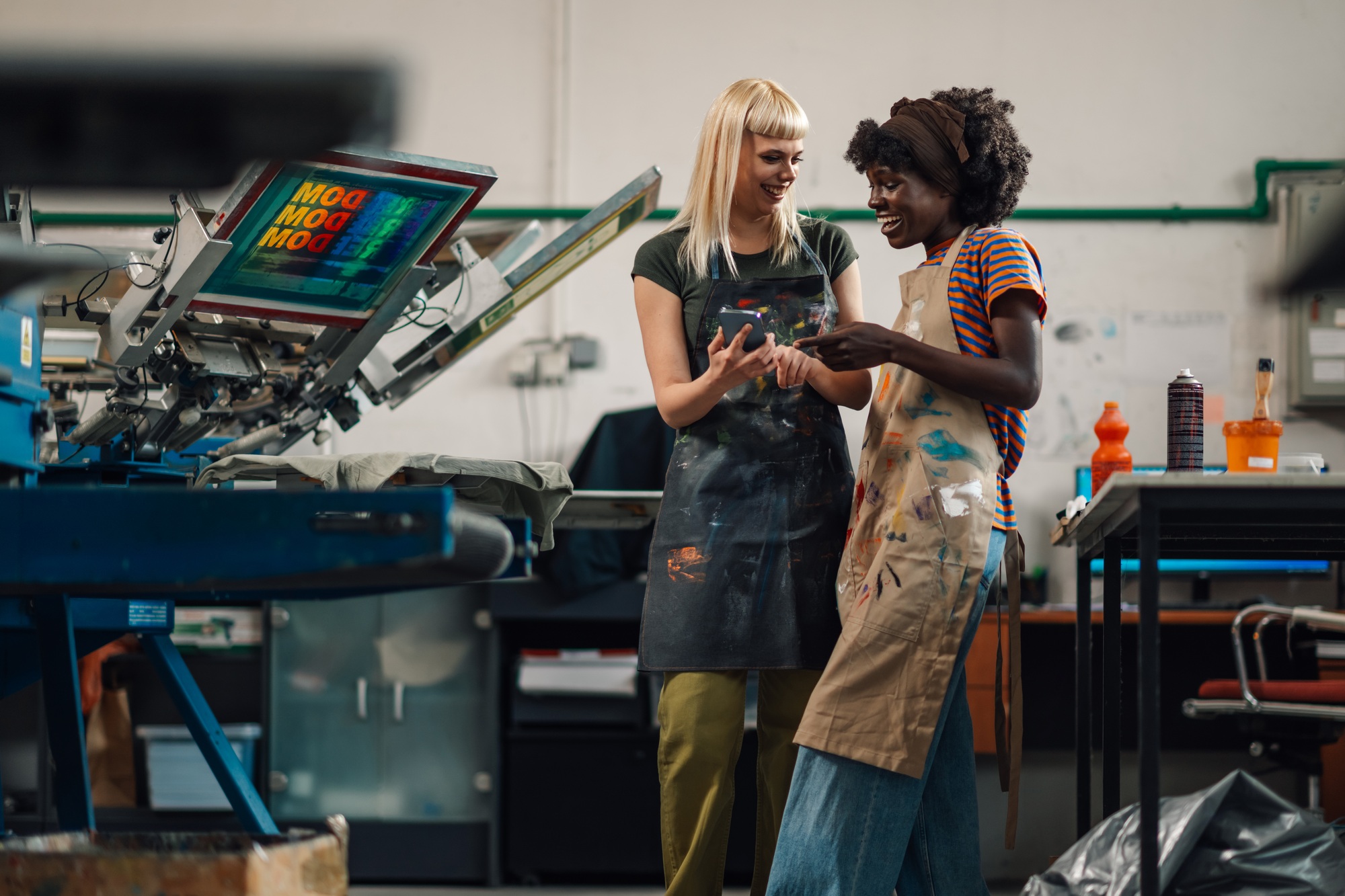 Interracial female graphic technicians smiling at phone at facility.