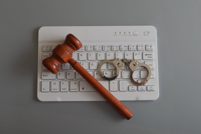 Judge gavel, laptop keyboard and handcuffs. Online scam, fraud, arrest and criminal concept.
