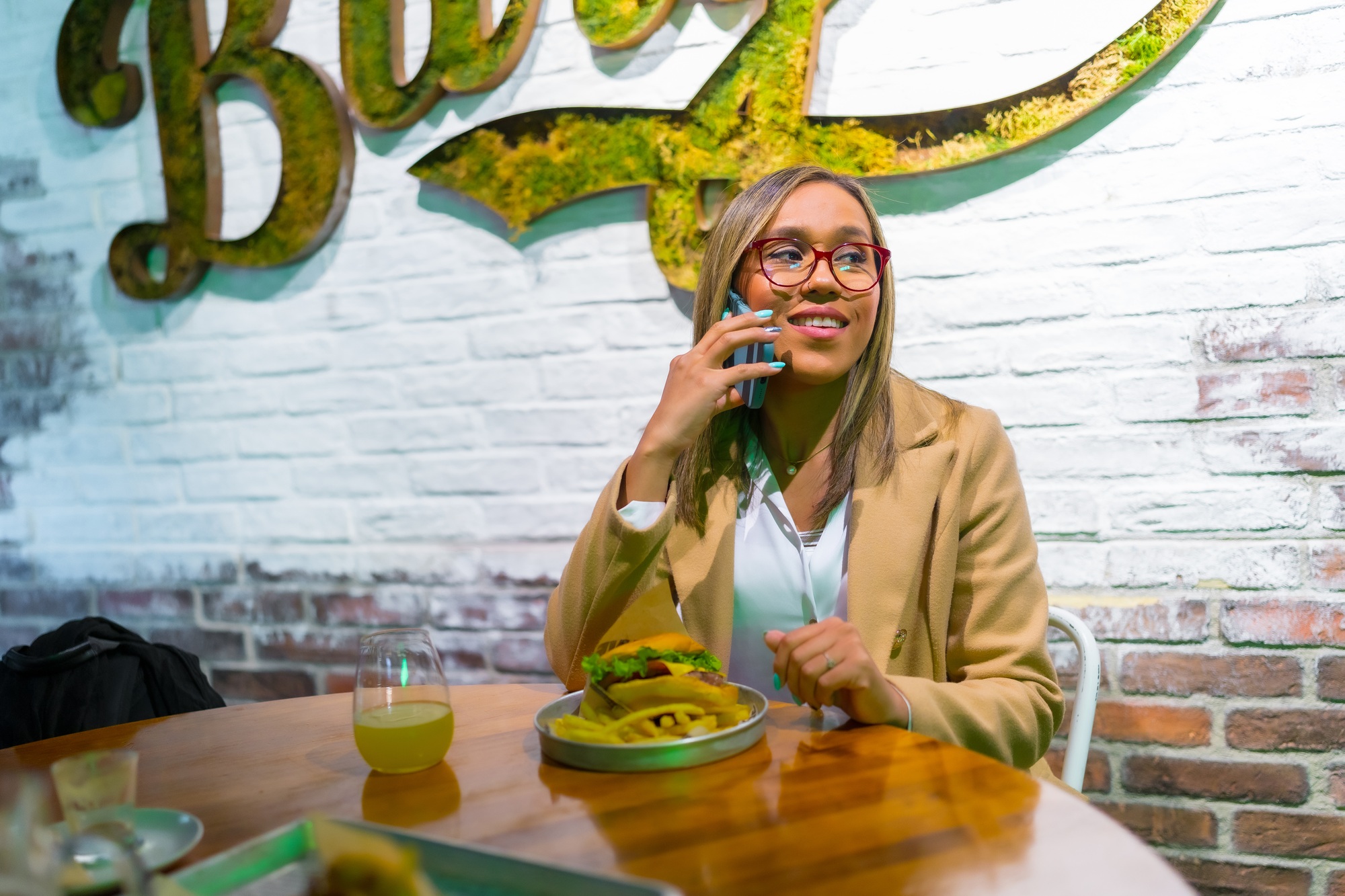 Latin woman talking to the mobile while eating burger