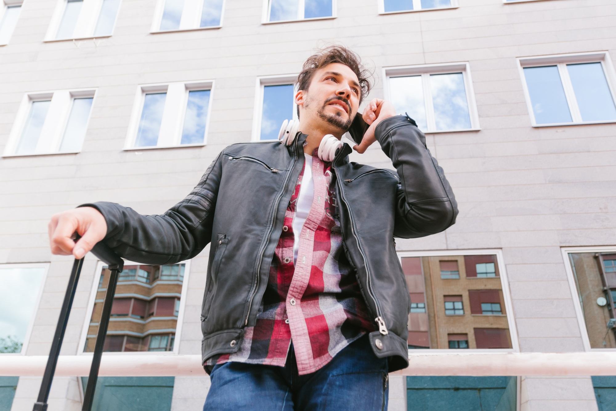 Low angle image of an adult man with a travel suitcase, talking with the smart phone