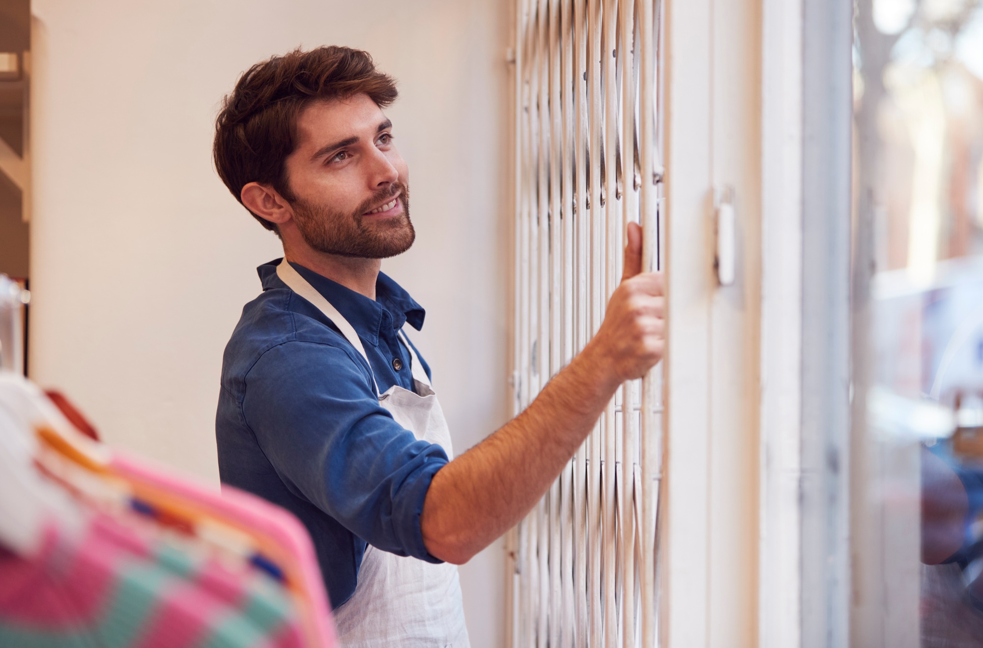 Male Small Business Owner Pushing Back Security Grill And Opening Shop