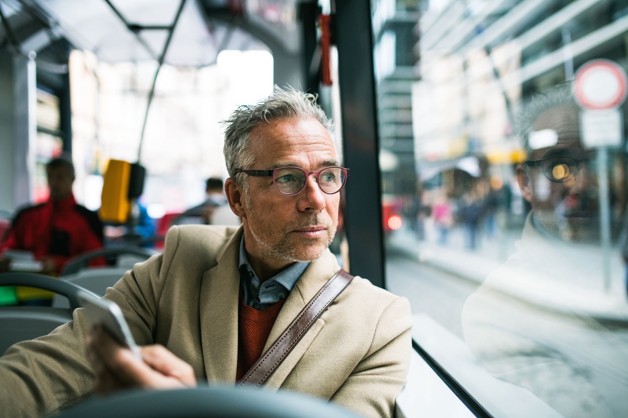 Mature businessman with smartphone travelling by bus in city.