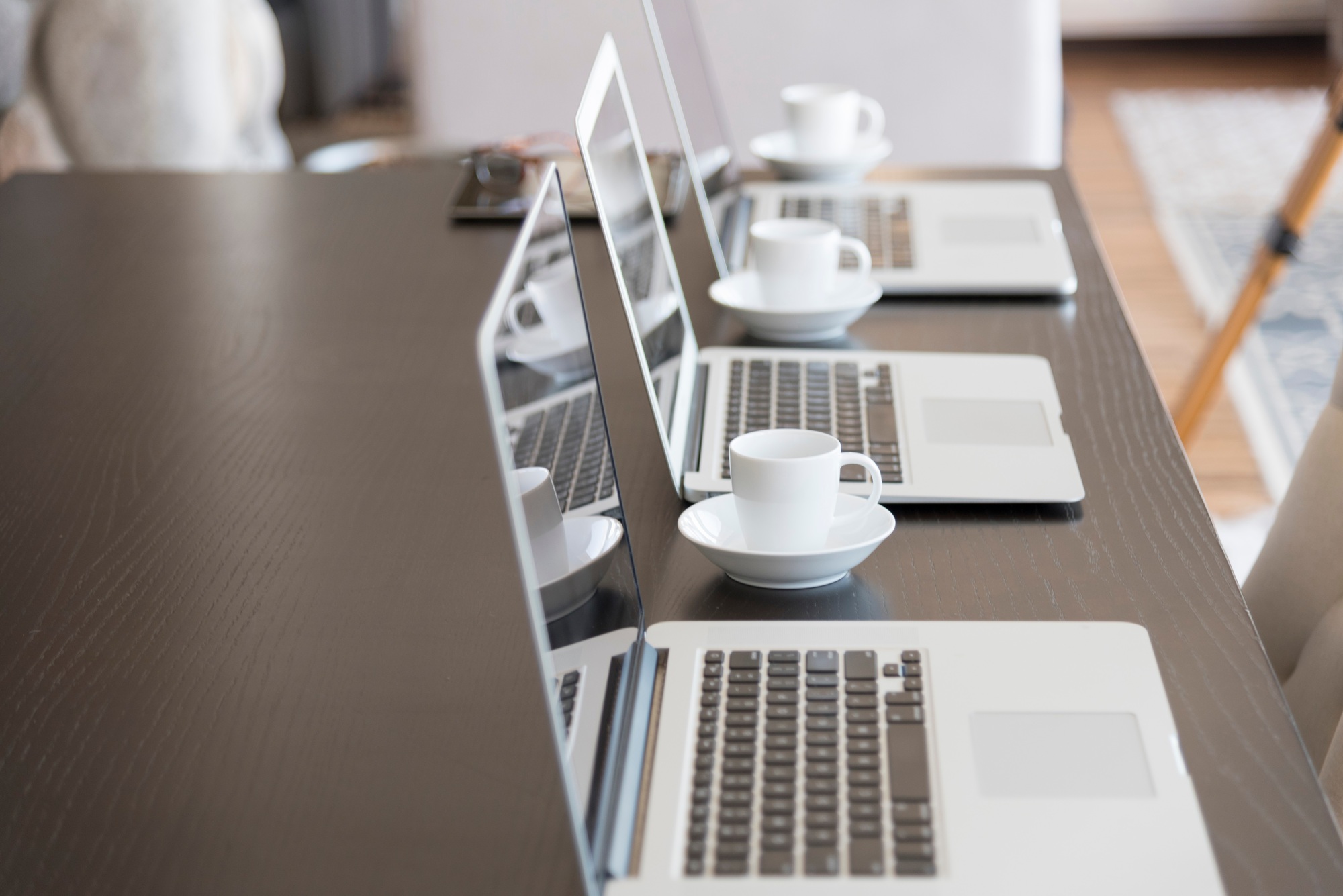 Multiple computers on conference table with lines of code and cups of coffee.