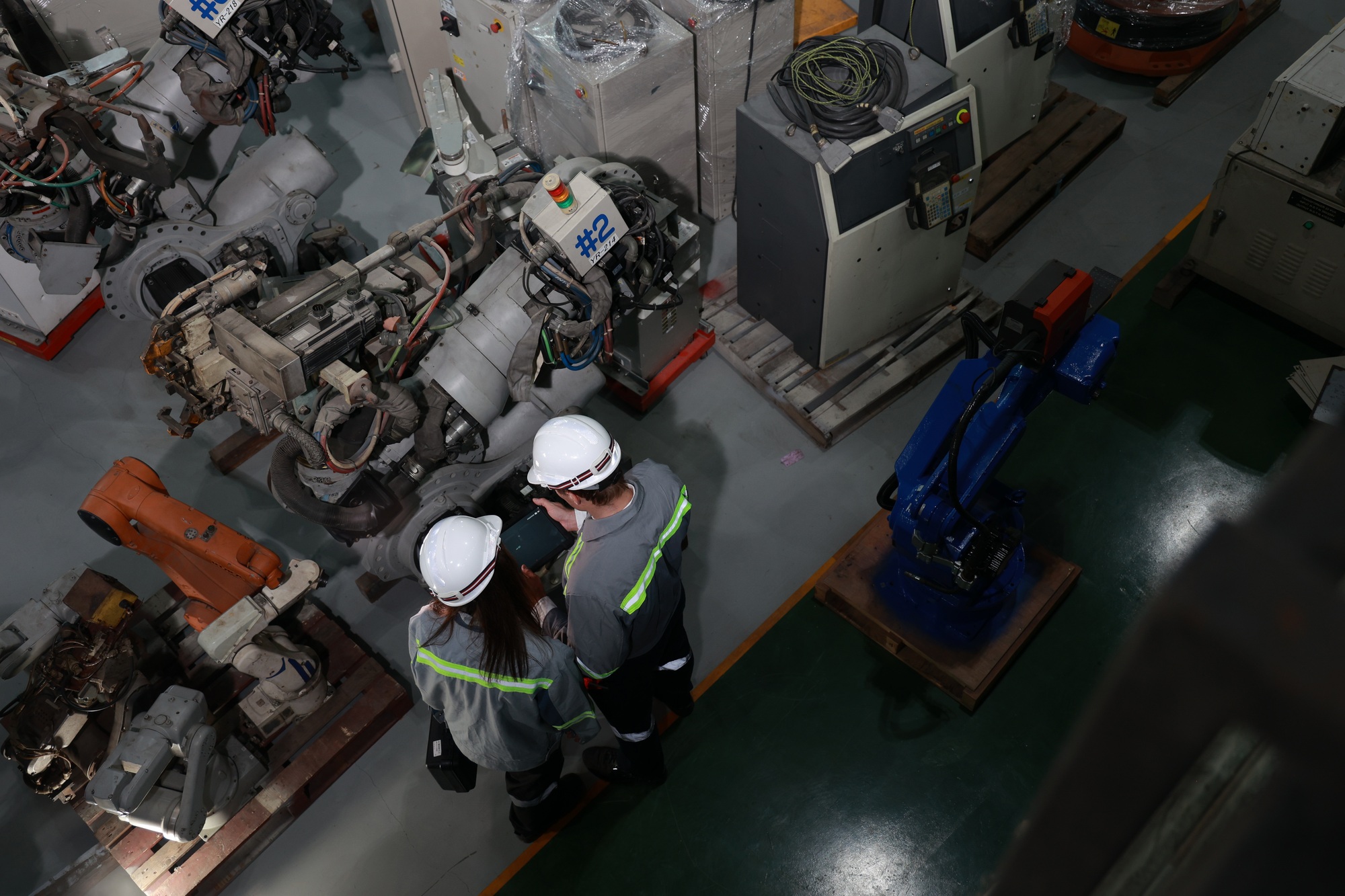 Overhead shot of two workers in hard hats analyzing production in a machinery-filled factory floor