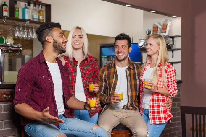 People Friends Drinking Orange Juice Talking Laughing Sitting At Bar Counter, Mix Race Man And Woman