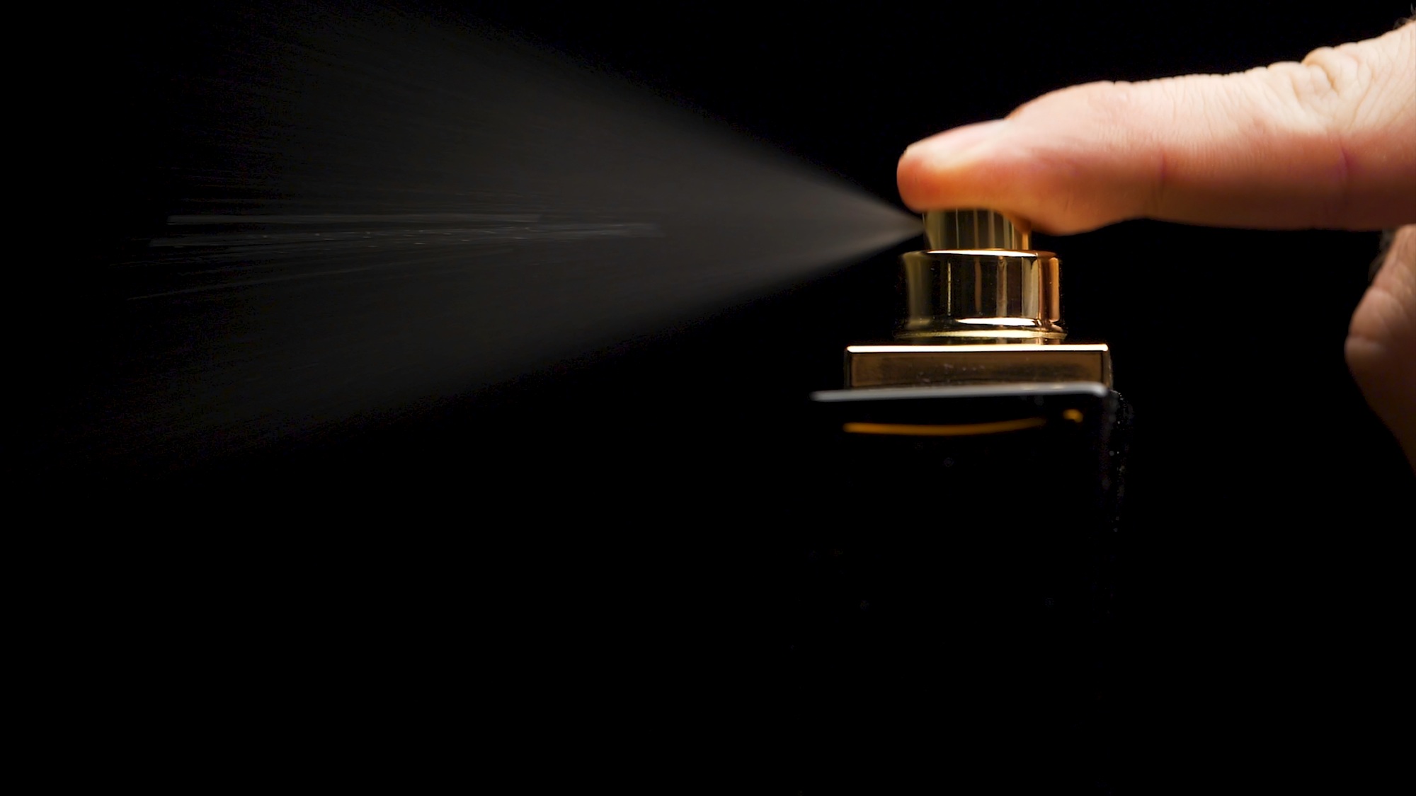 Perfume bottle with male finger on black background. Man applying Perfume. Man's Perfume in the Hand