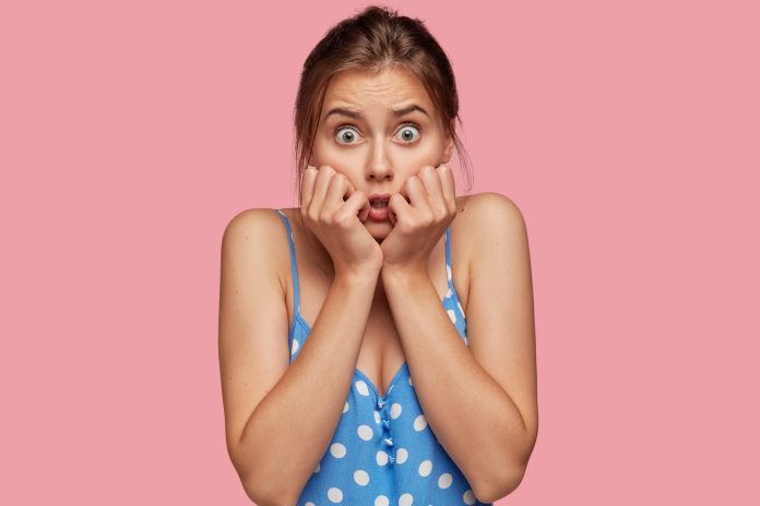 Photo of scared woman keeps hands near mouth, looks with fearful expression, cant believe in failure