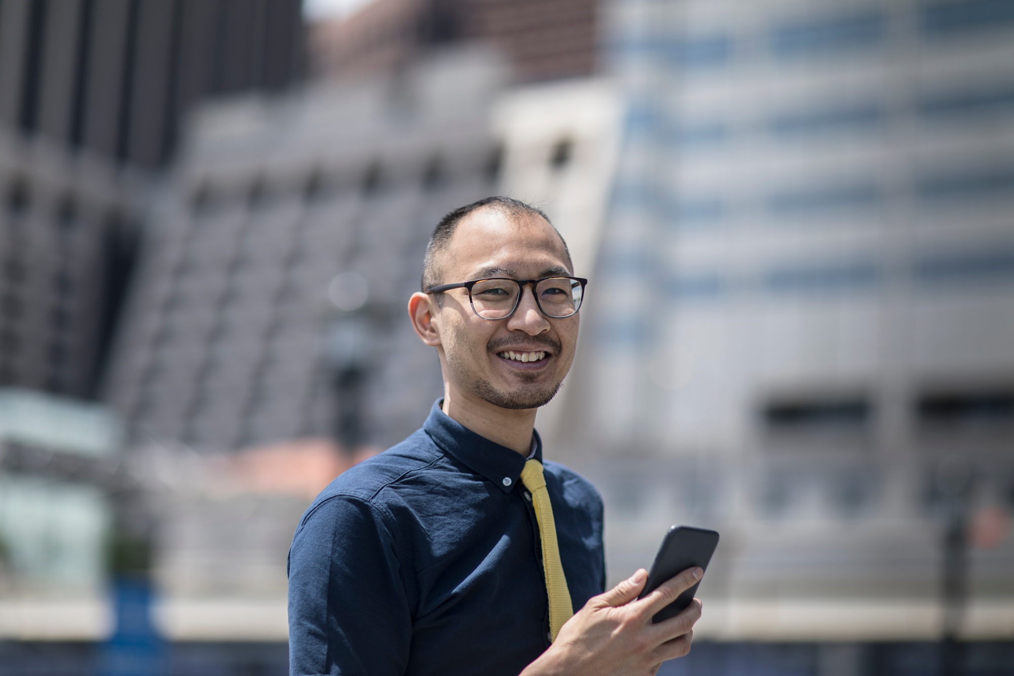 Portrait of smiling businessman with smartphone outside office building, New York, USA