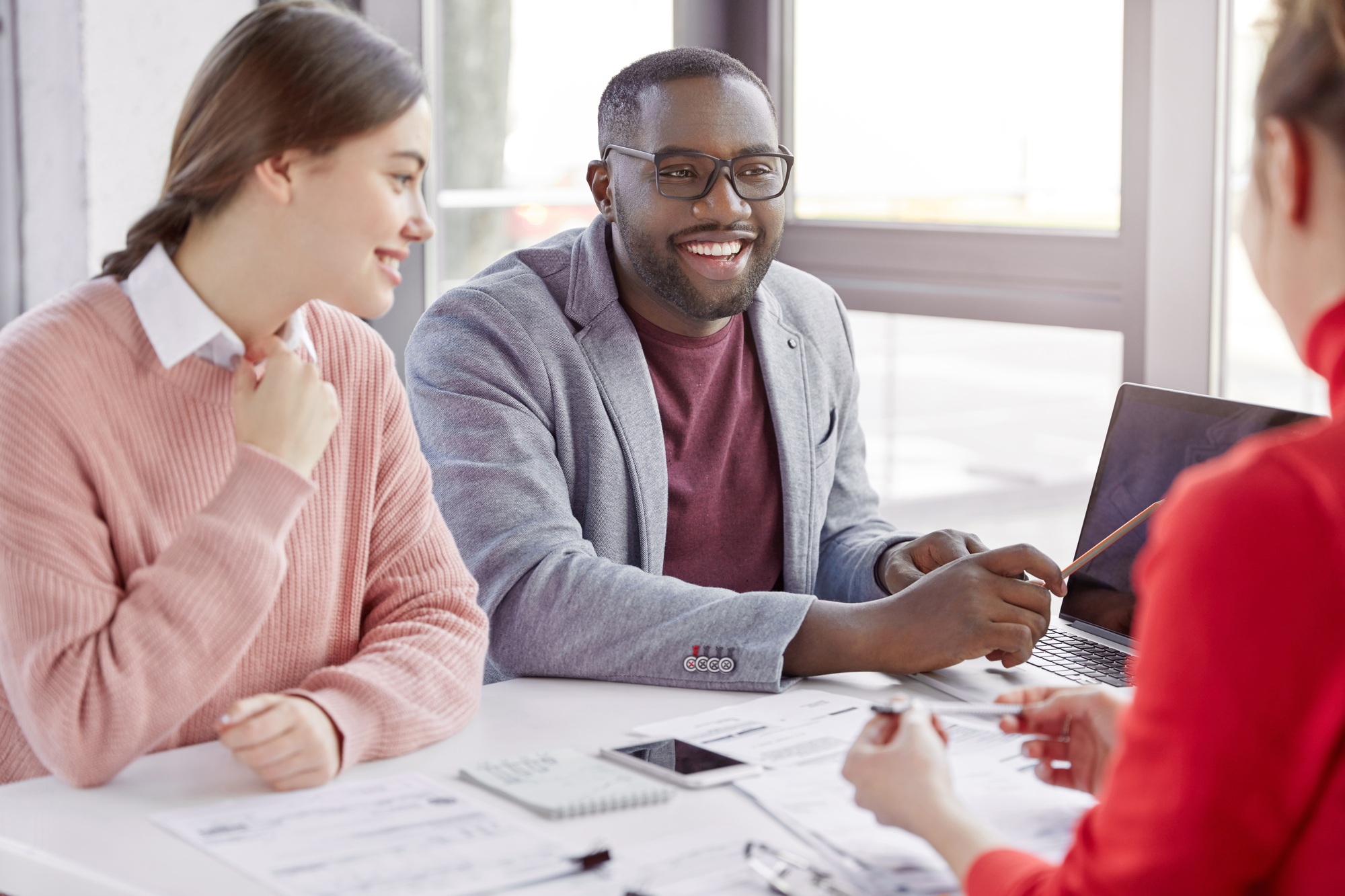 Professional black male coach explains to female employees strategy, points at laptop computer, have