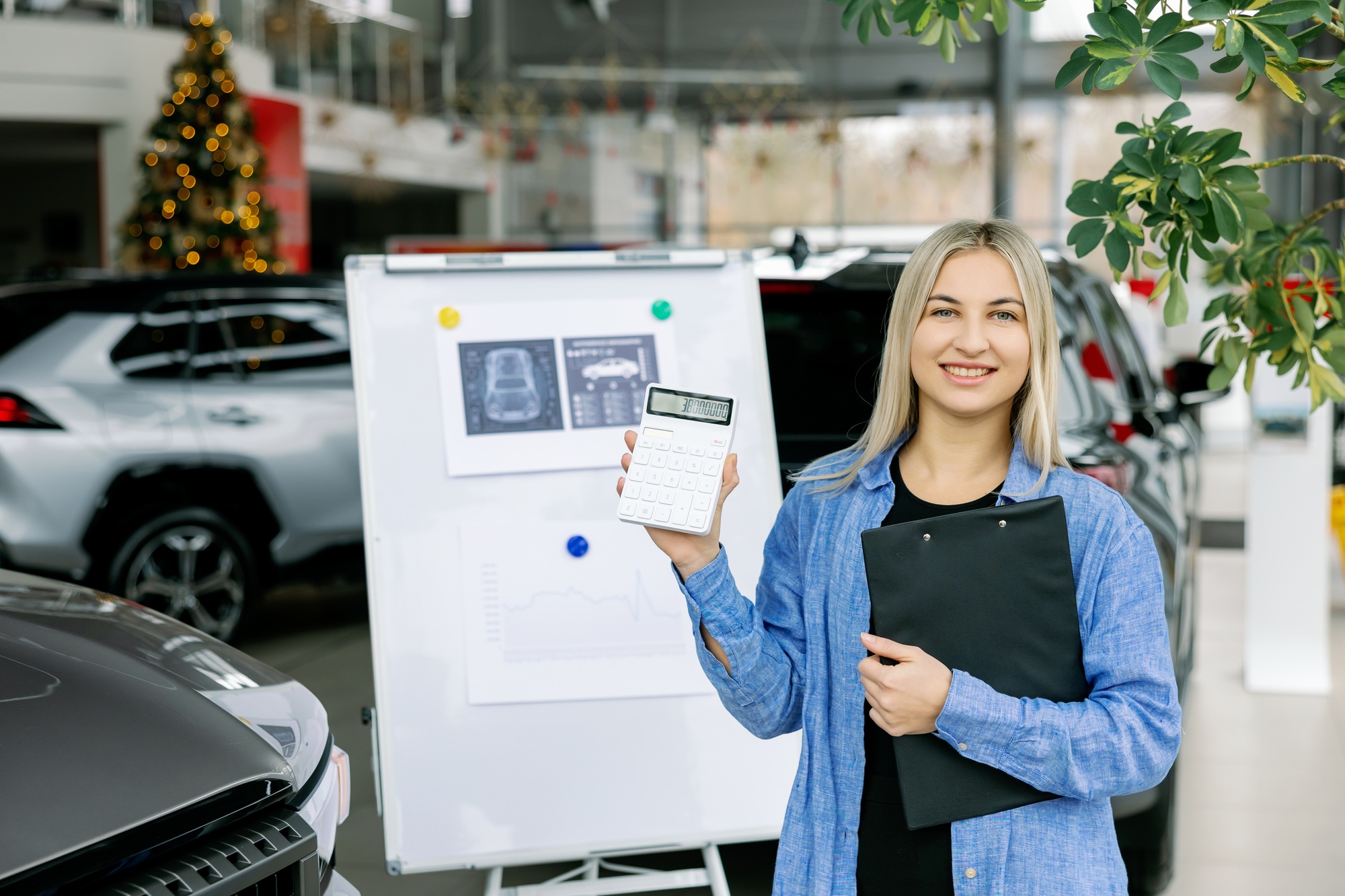 Saleswoman showing calculator and clipboard in car dealership