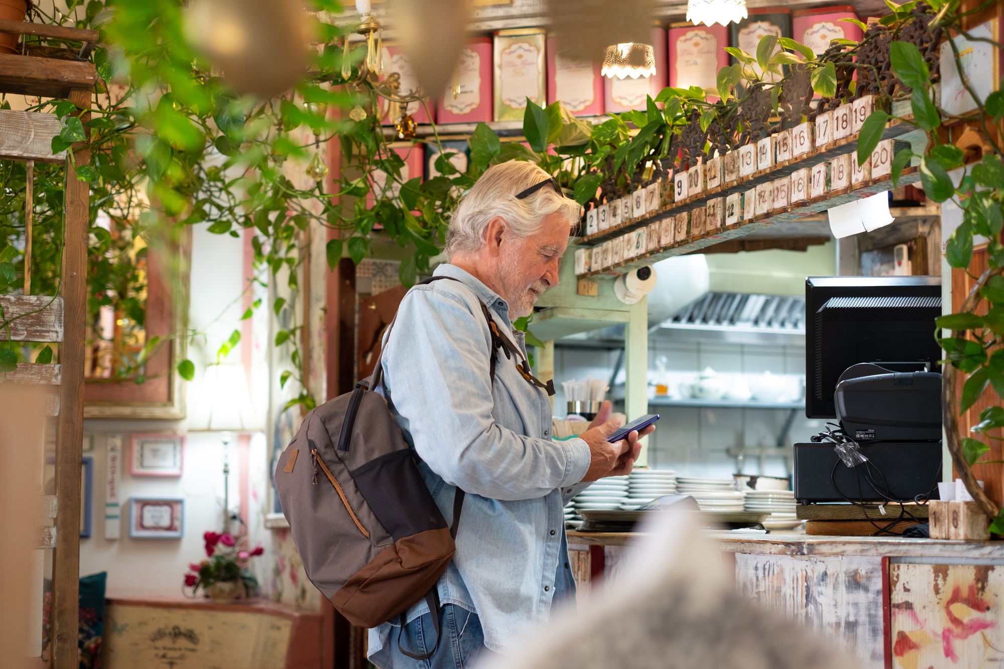 Senior white-haired man pays at the coffee shop checkout using the application on his mobile phone