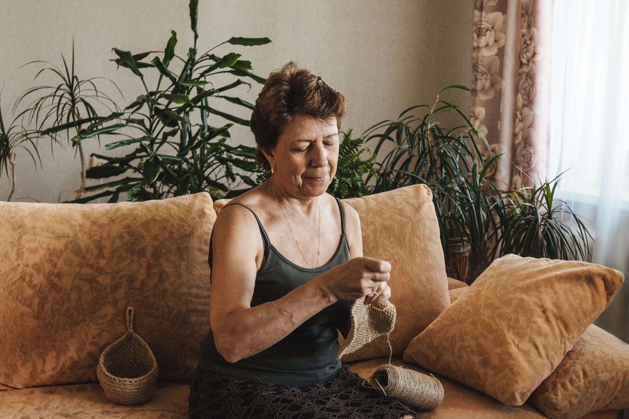 Senior woman crocheting napkin from natural thread.