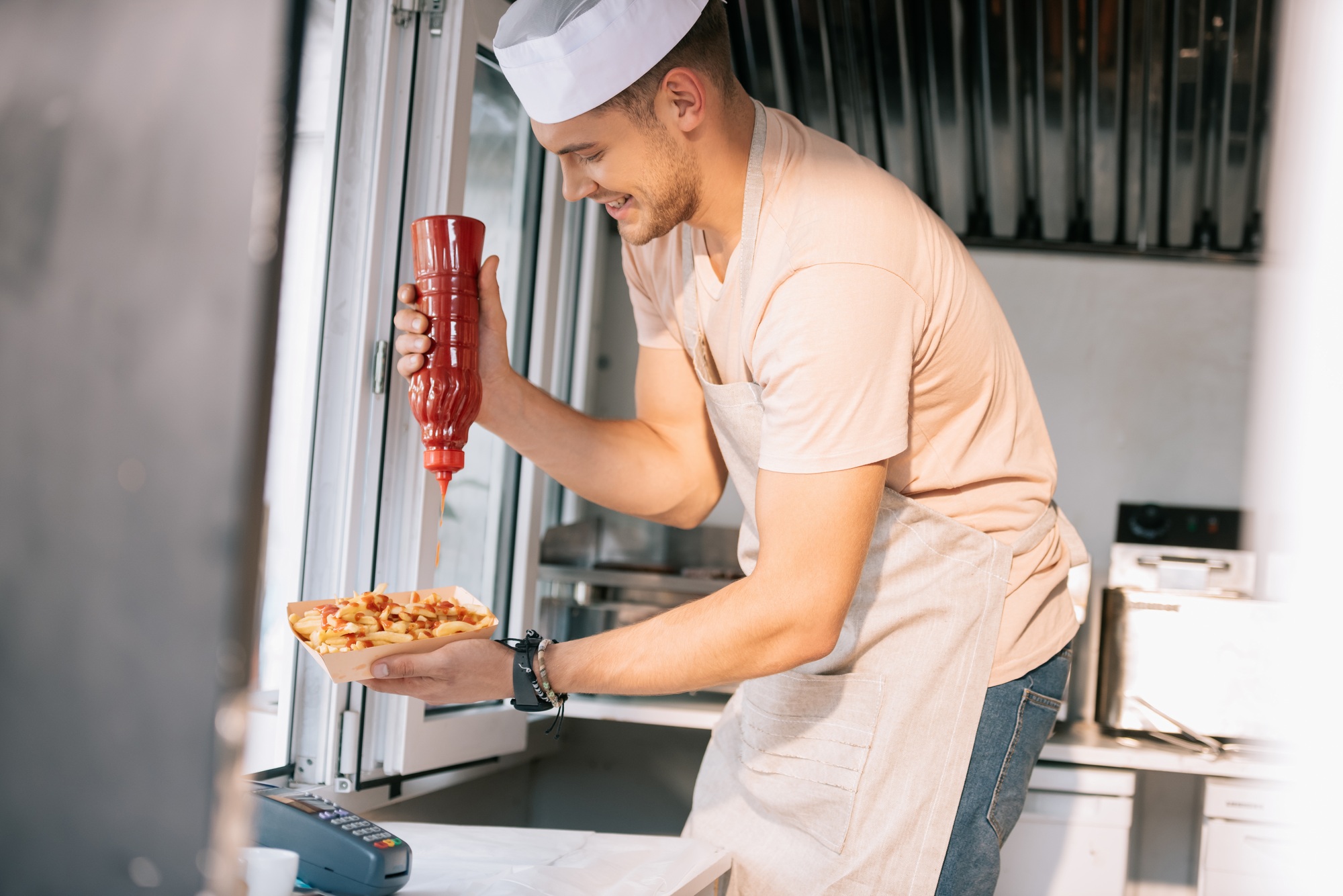 side view of chef adding ketchup to hot dog in food truck