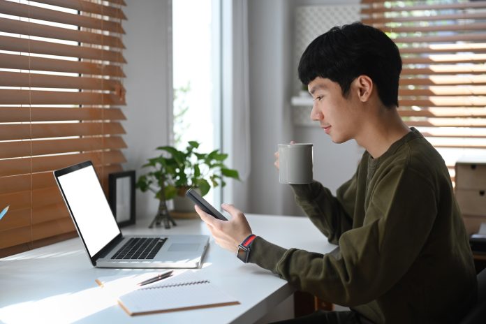 Side view of young businessman drinking coffee an checking social media on mobile phone.