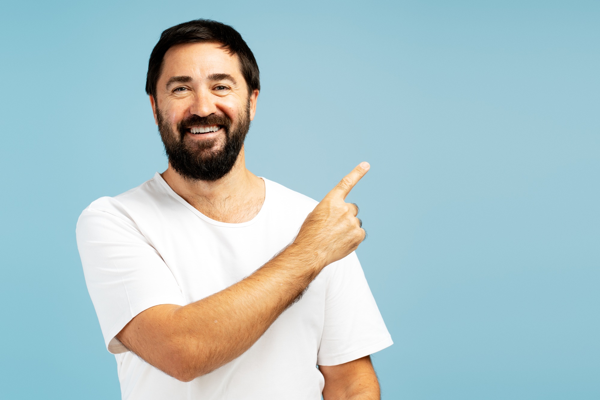 Smiling bearded man pointing finger showing something on blue background