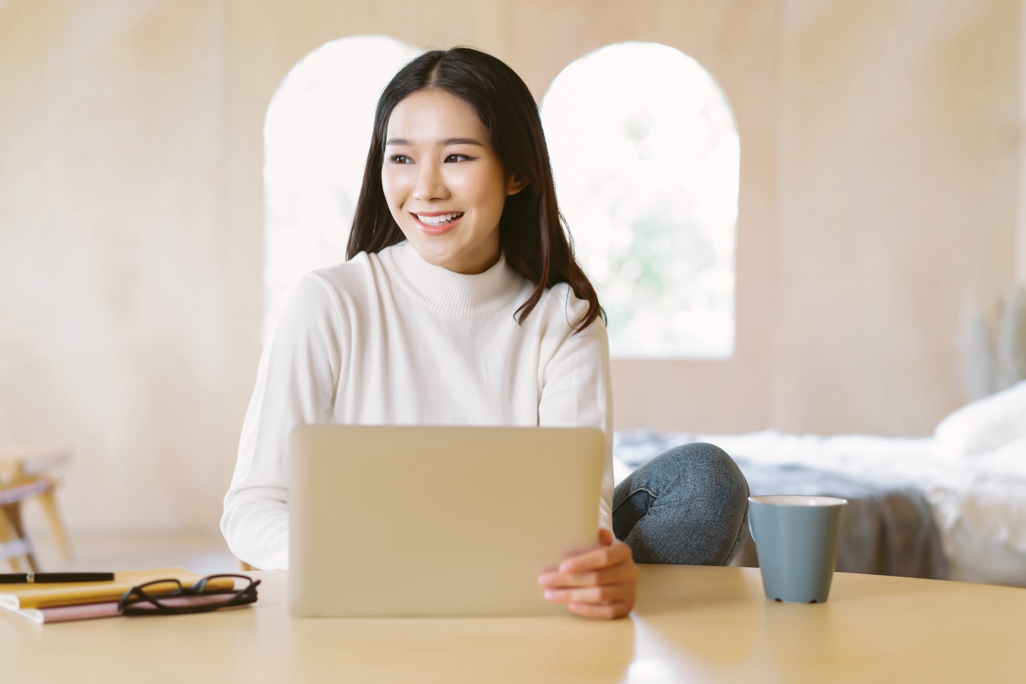 smiling freelancer Asian woman work remotely on laptop and looking away in home winter atmosphere.