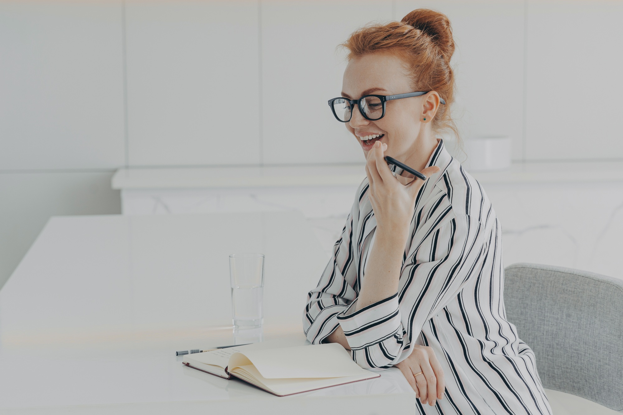 Smiling woman holding mobile and speaking with virtual digital voice recognition assistant at home