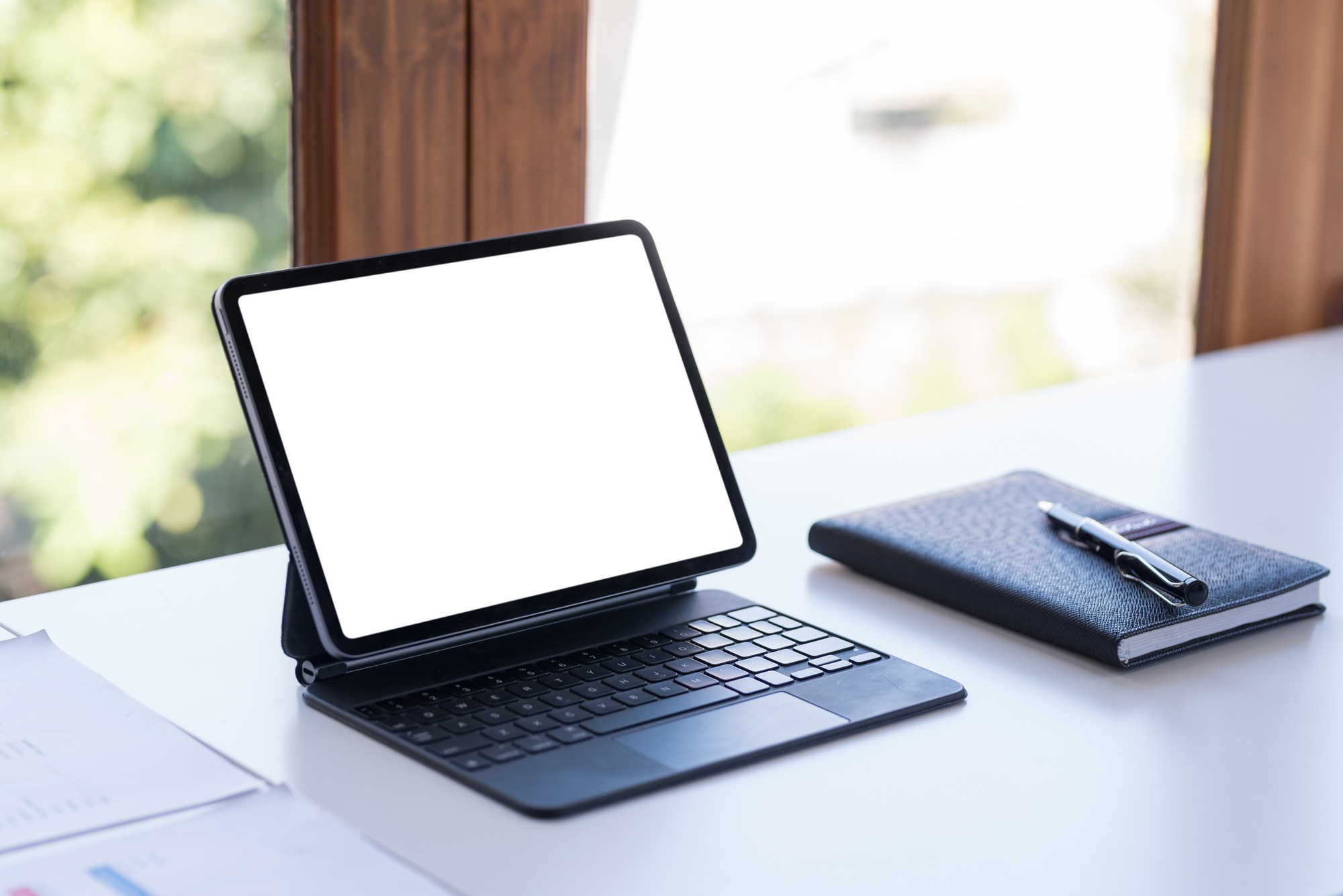 Tablet is displaying a white screen for your advertisement on a work desk with a notebook