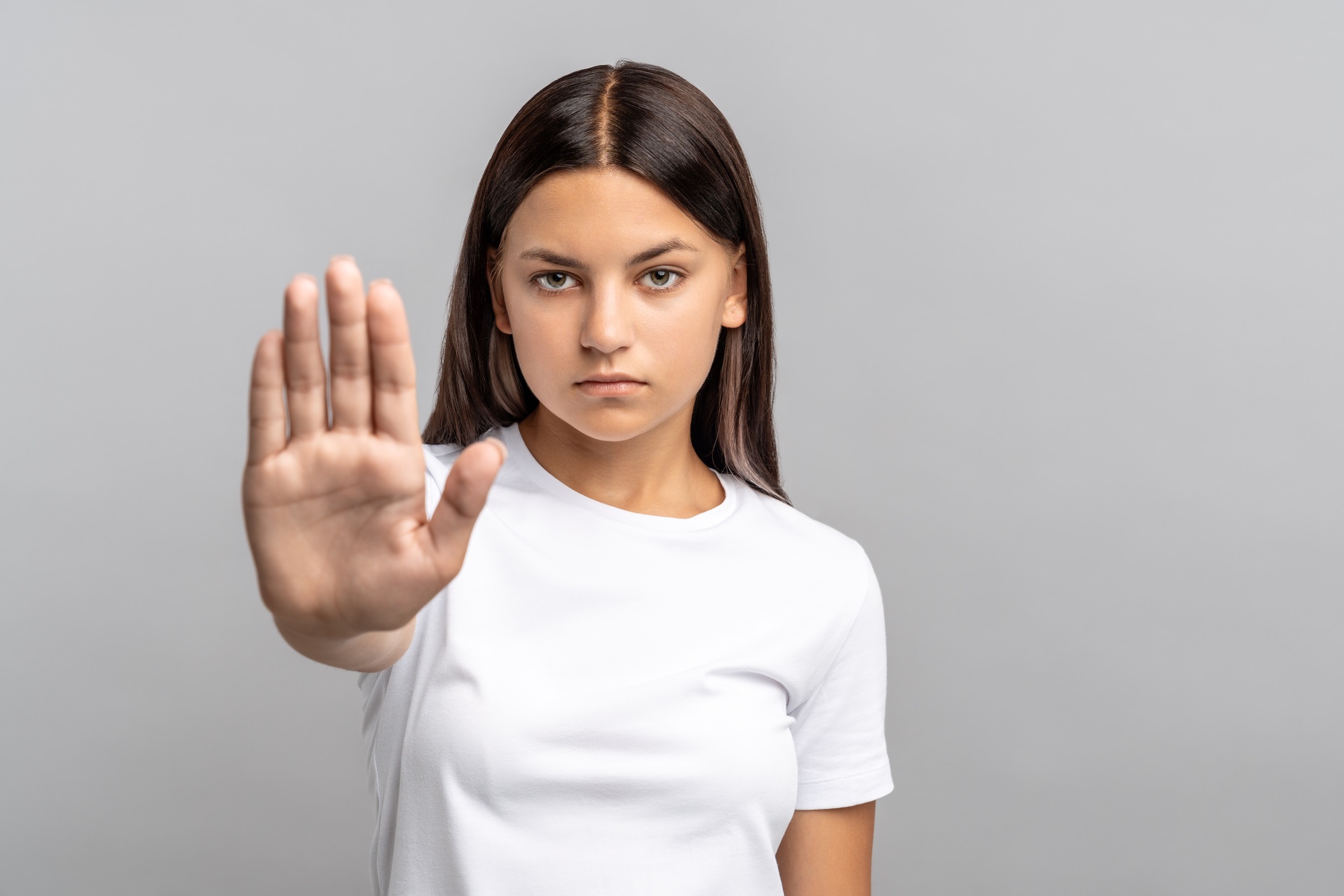 Teenager girl extends hand in stop gesture, confident, overcoming fears and social pressures