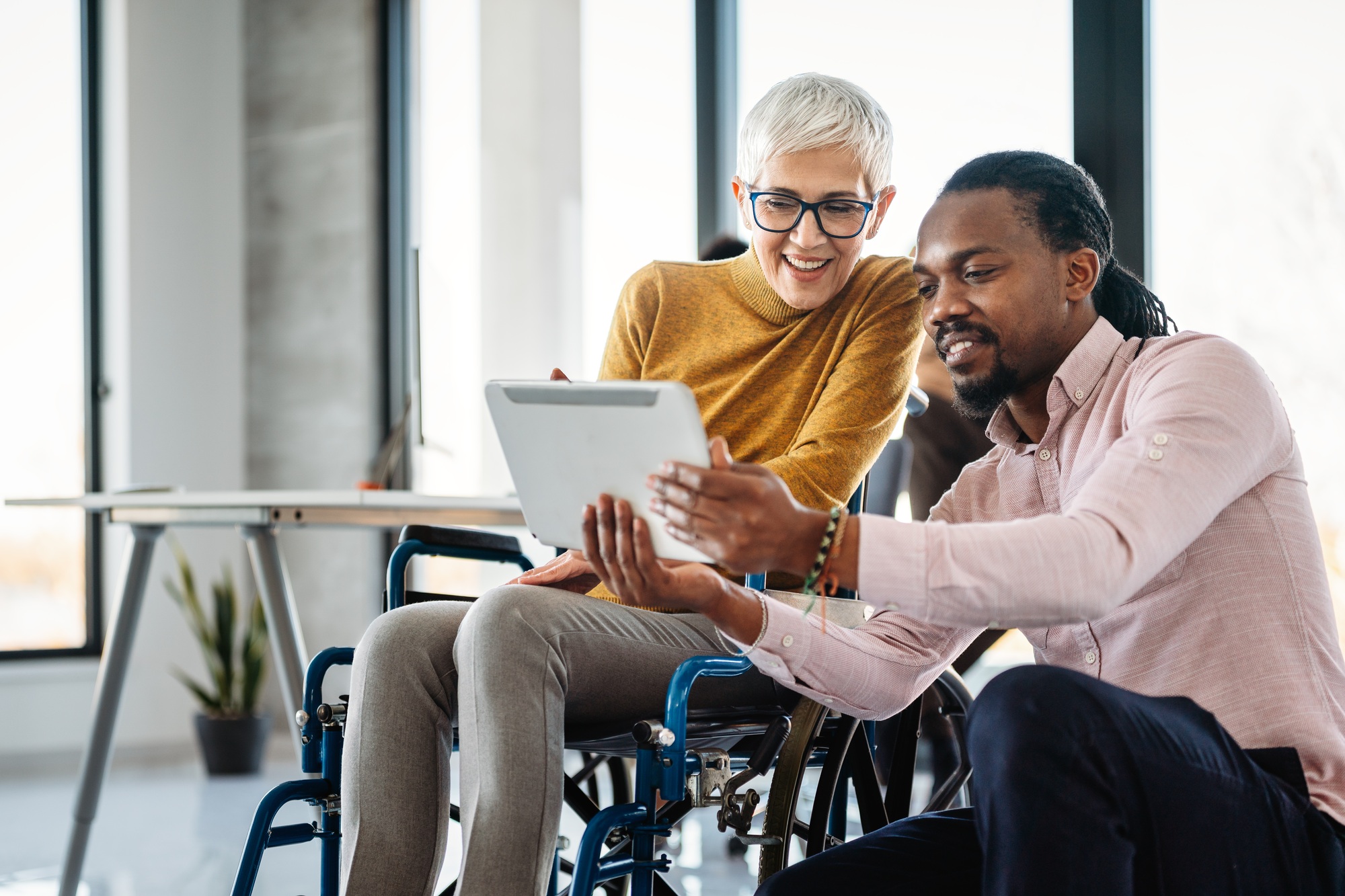 The image includes a person using a wheelchair, depicting inclusivity and teamwork in modern office