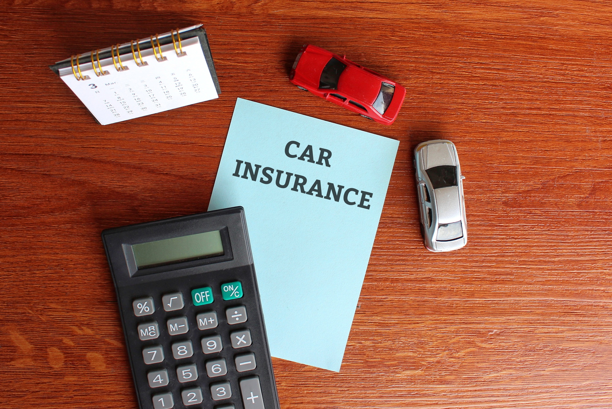 Top view of desk calendar, calculator, miniature car and paper with text CAR INSURANCE.