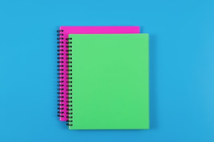 Top view of green and magenta spiral journals isolated on blue table background.