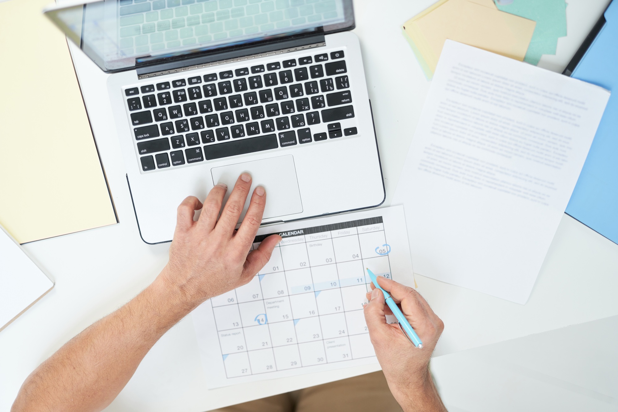 Top view of hands of man using his laptop and marking days in calendar