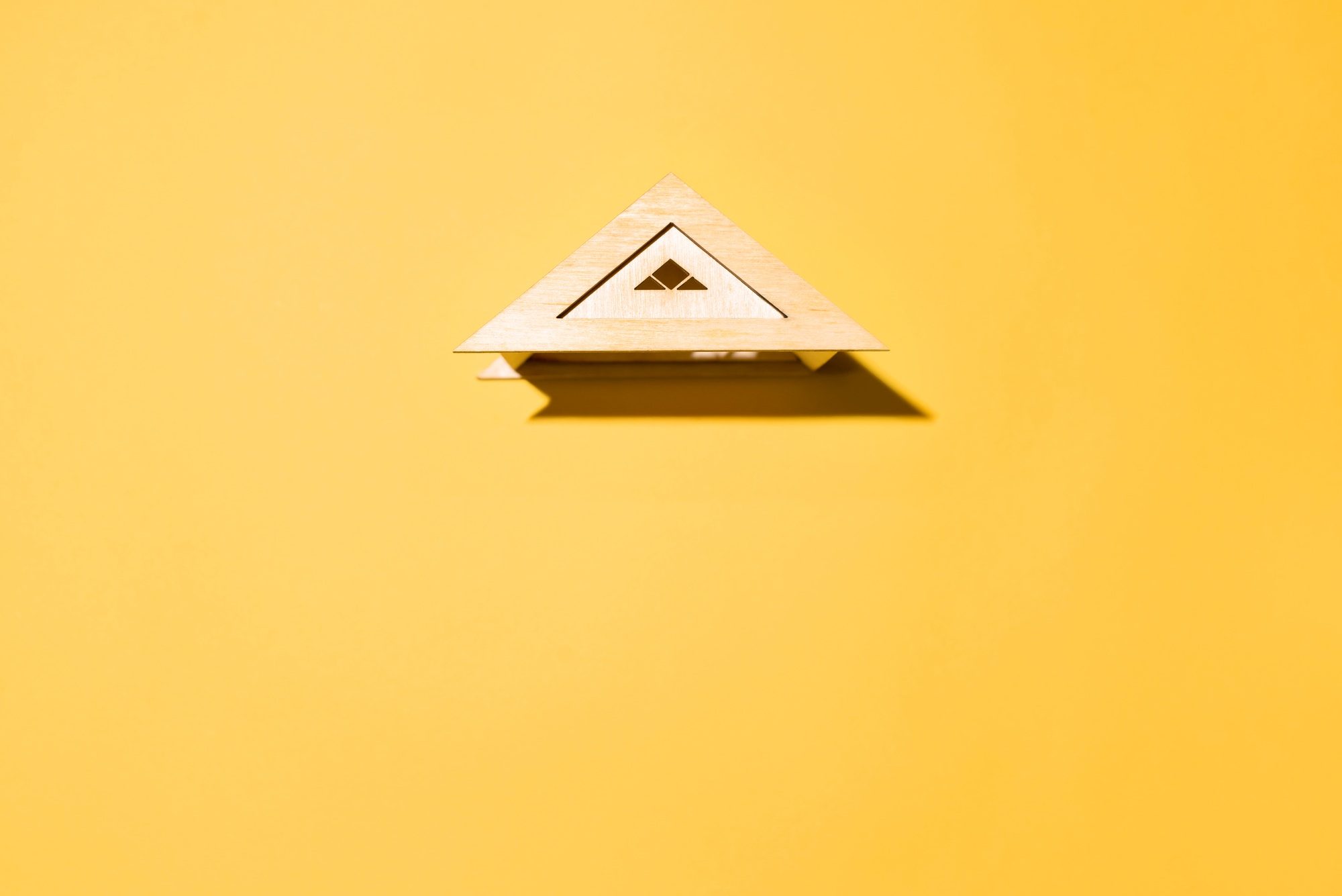 Toy wooden roof on yellow background top view, copy space. Housing concept, insurance, ad space