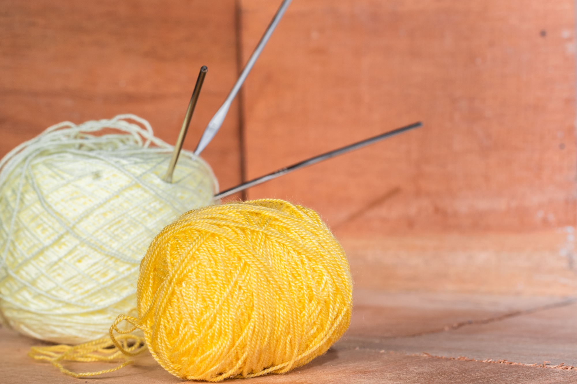 two rolls of yellow and white yarn to crochet, with needles stuck on them